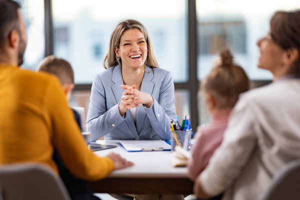 A woman in a blue blazer smiling and speaking with a group of people at a meeting or interview in an office setting.