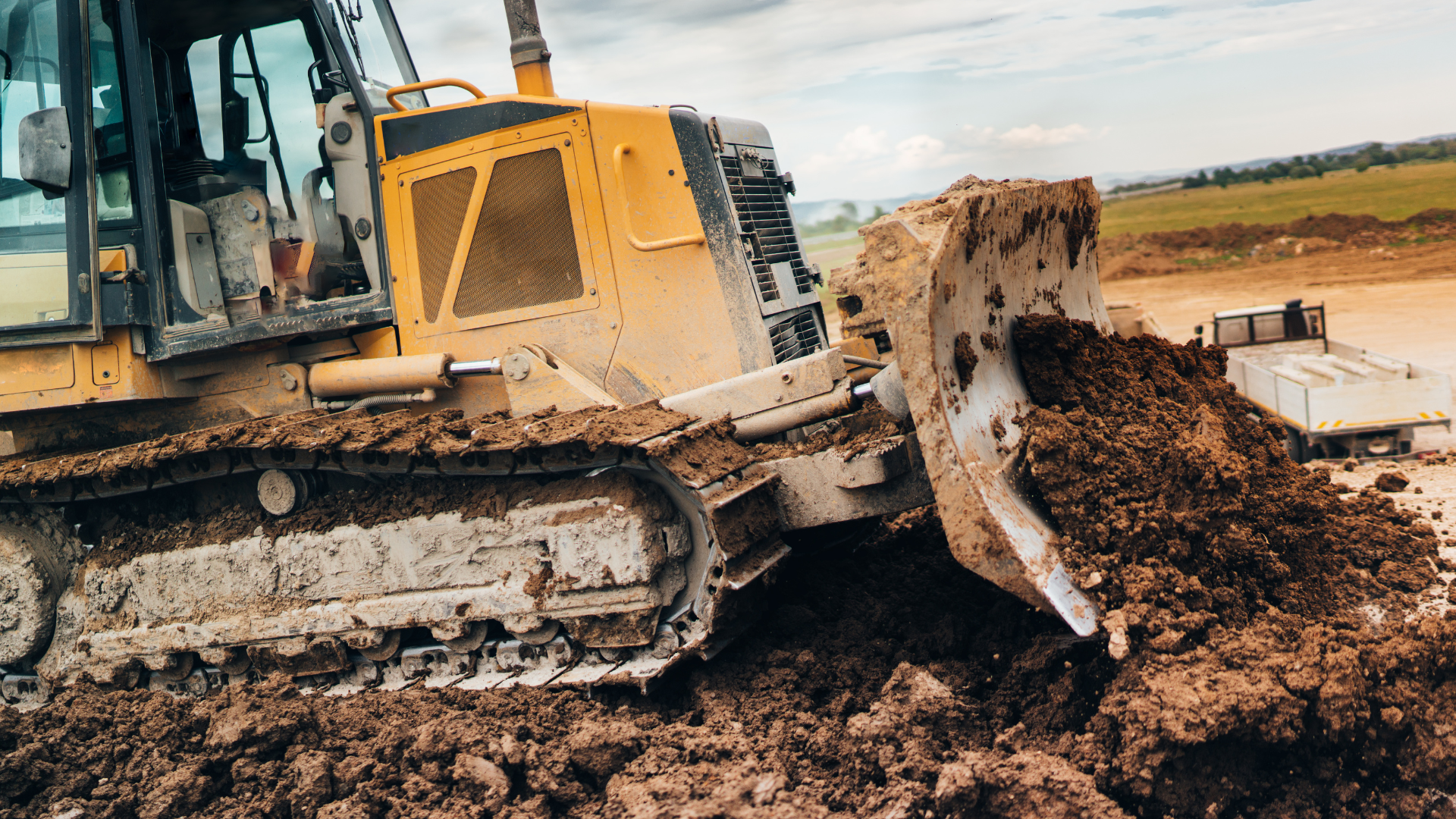 A yellow bulldozer pushing large amounts of soil on a construction site, with a tractor in the background and open land with grass and hills. Bulldozer for kids. Construction show for kids. 