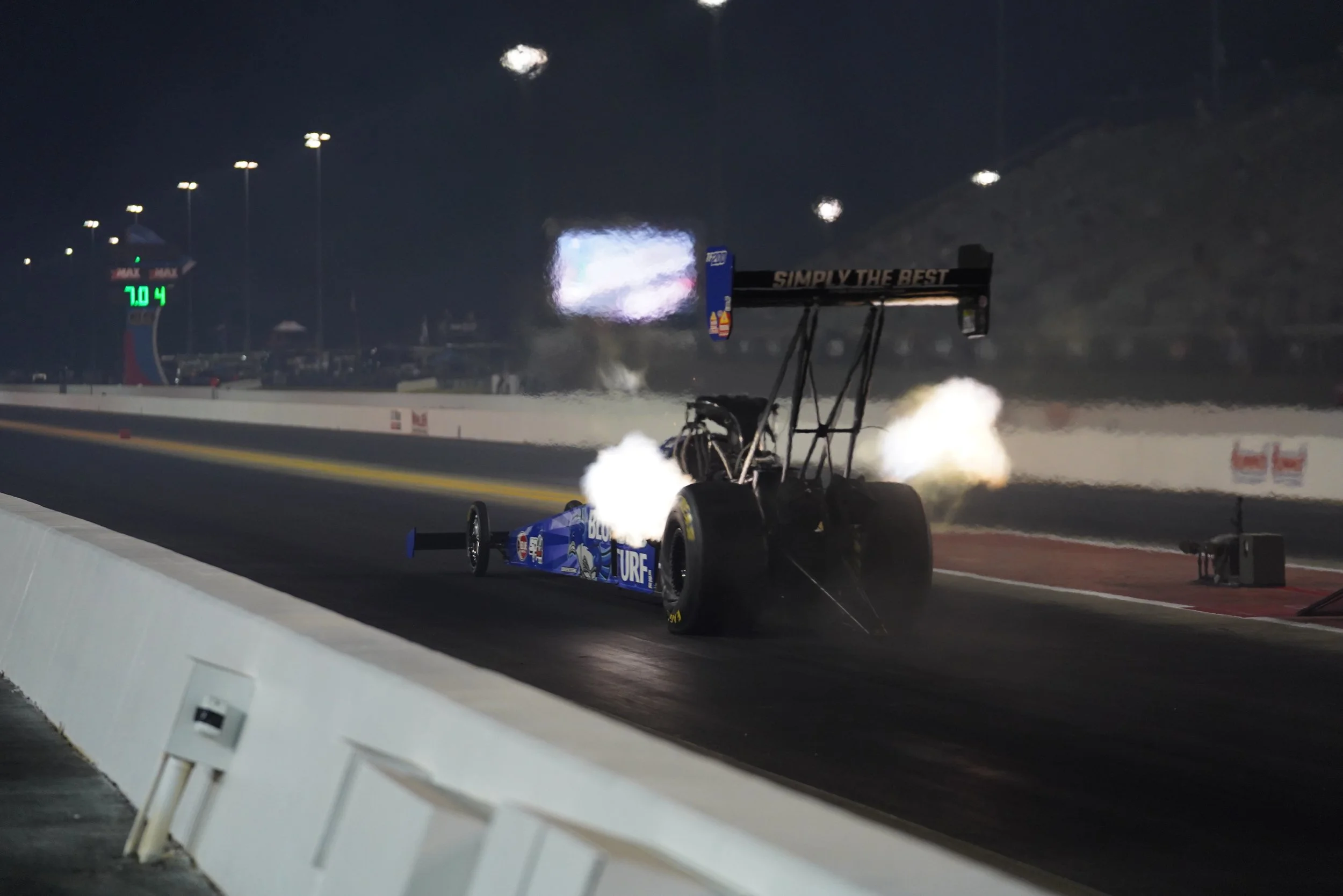 A blue drag racing car on a track at night. BTS of The Mr. Machine Show. Behind-the-Scenes of The Mr. Machine Show with Tay Whiteside. NHRA Drag Racing for kids. Jasmine Salinas on The Mr. Machine Show. 