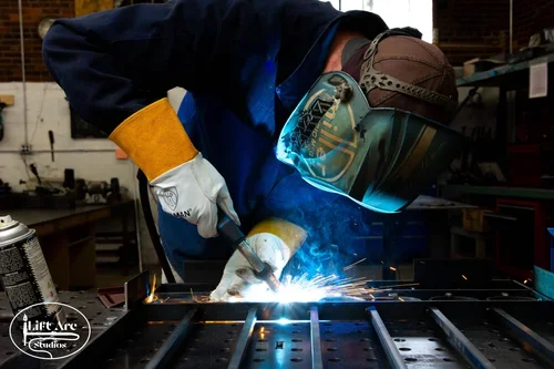 A person welding metal in a workshop, wearing protective gear including a helmet and gloves. Tay Whiteside as a professional welder. Mr. Machine in real life.