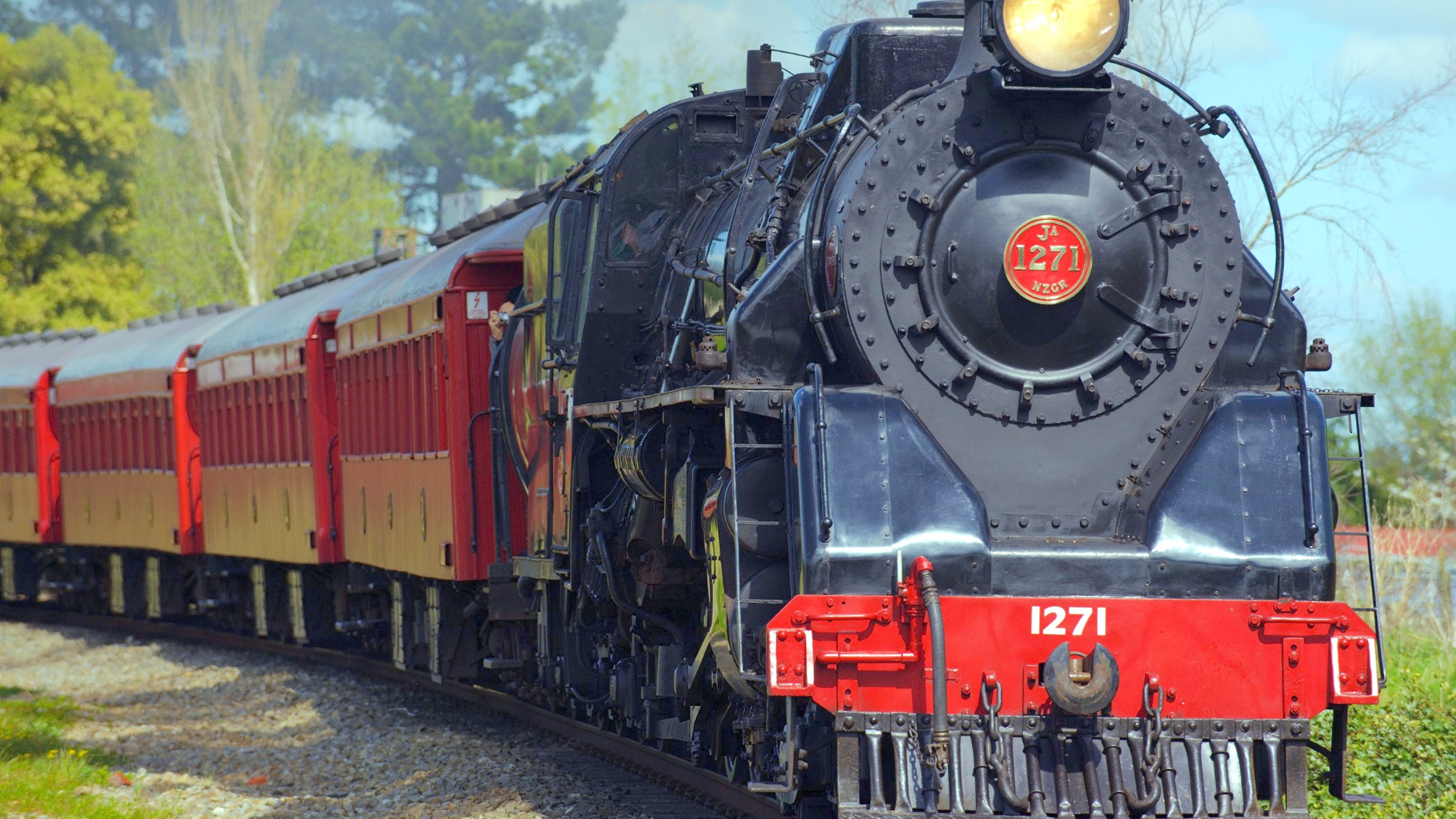 A steam locomotive train with the number 1271 on its front, traveling on a curved railway track with green trees in the background. Trains for kids. Trains show for kids. 