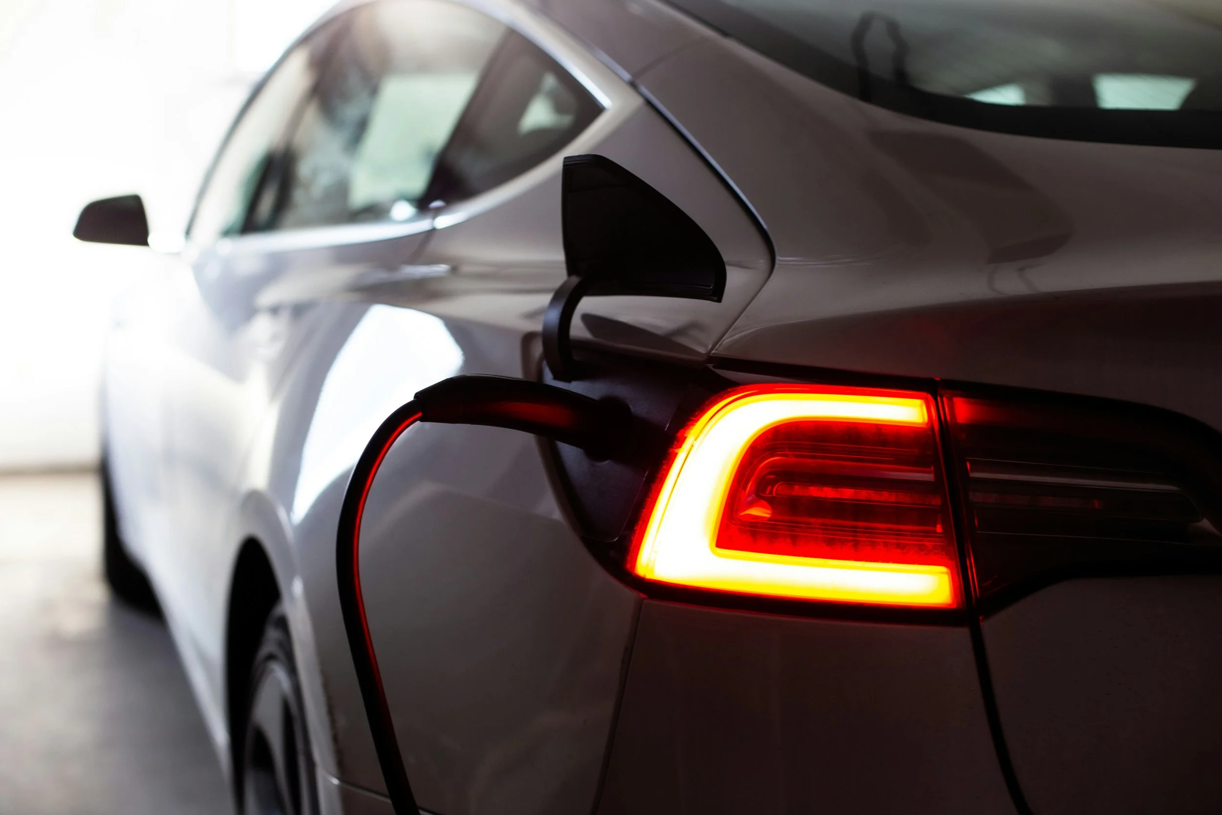 Close-up of a silver car showing the rear left side, tail light illuminated with brake lights, and an open trunk.