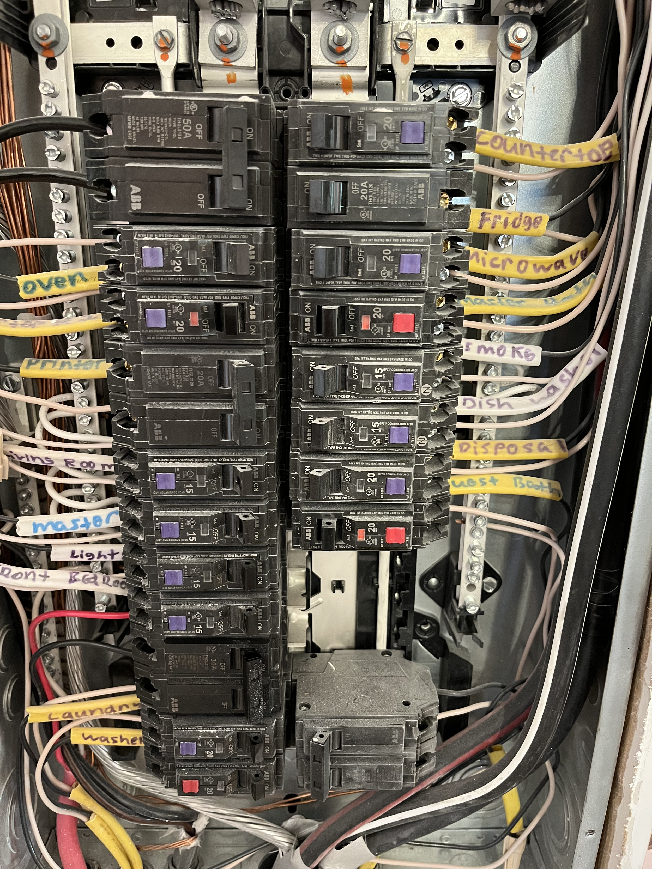 An electrical fuse box with multiple fuses and circuit breakers, labeled with white, yellow, and purple tags indicating their functions, such as furnace, microwave, dishwasher, washer, and lights.
