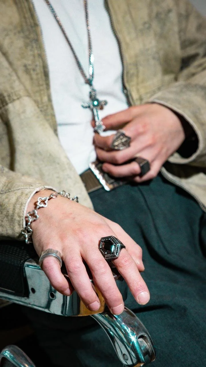 Hombre usando múltiples anillos, brazalete, y collares de plata 
