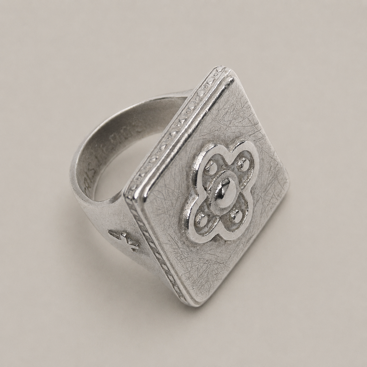 Anillo de plata con una cara cuadrada que presenta un diseño floral en el centro.