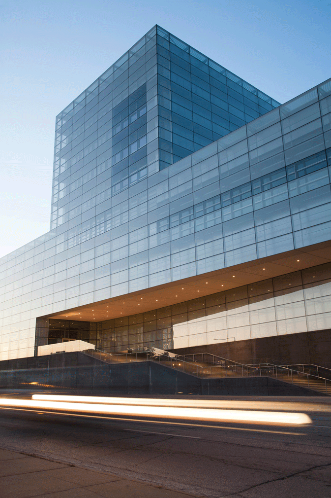 Modern glass office building reflecting the sky and surroundings during sunset, with moving vehicles in the foreground.