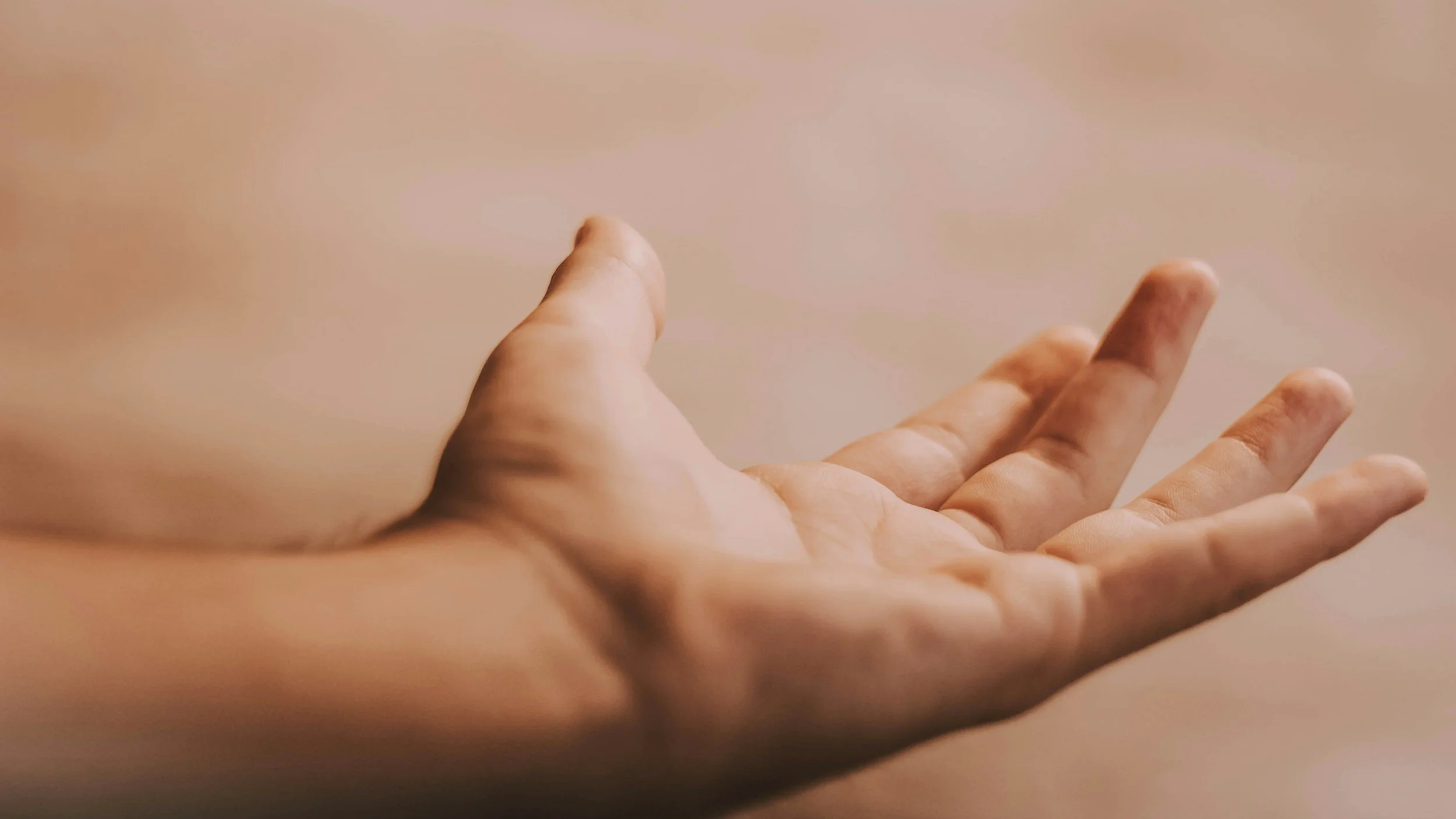 Close-up of two hands with fingers slightly spread, positioned over a plain, neutral background.