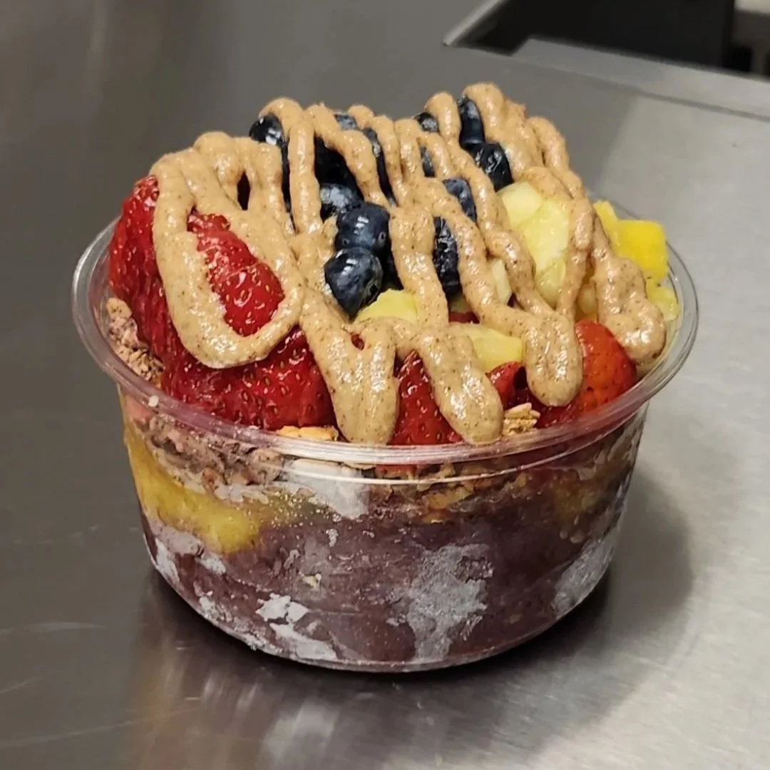 A clear plastic cup filled with layered fruit, topped with strawberries, blueberries, pineapple, and a beige drizzle of sauce or dressing.