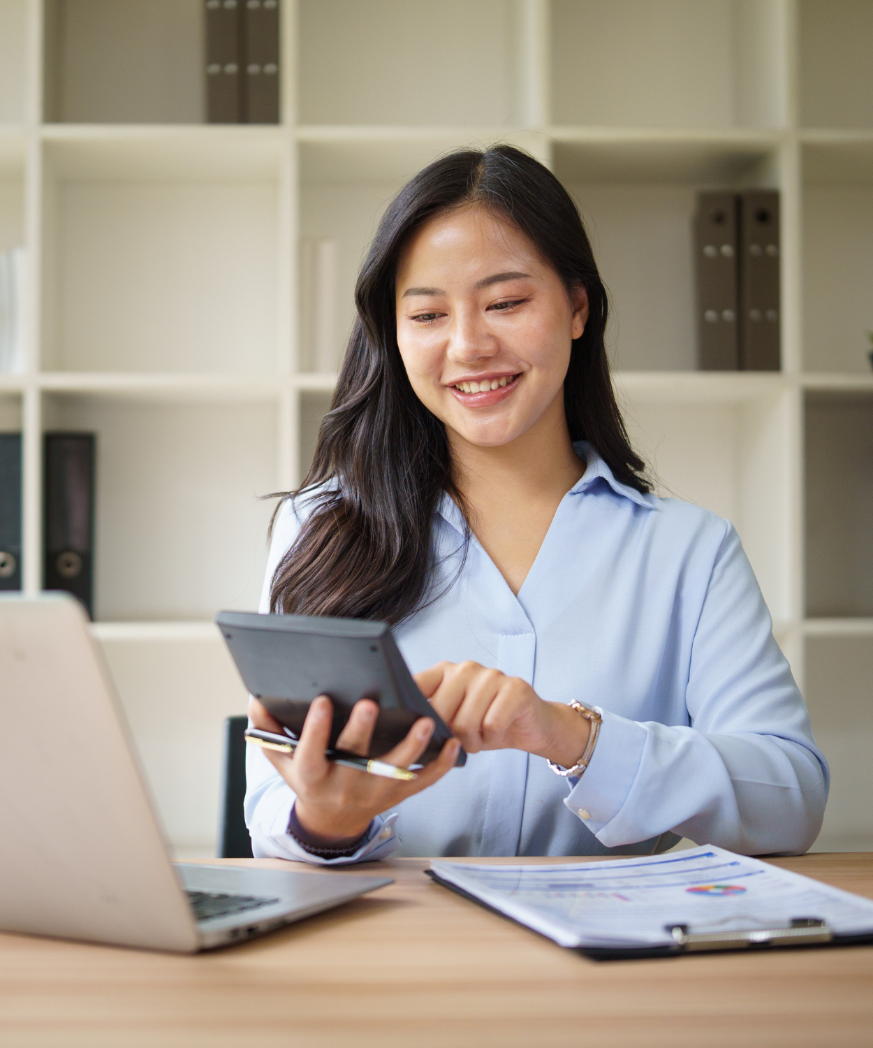 A woman with long dark hair smiling while looking at her phone in an office setting.