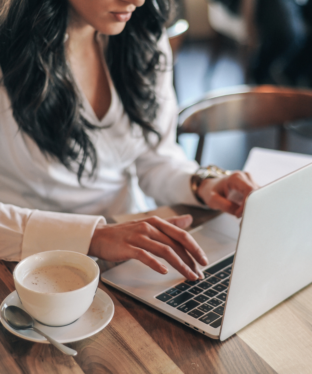 Two women working on a laptop at a wooden table, with a cup of coffee.