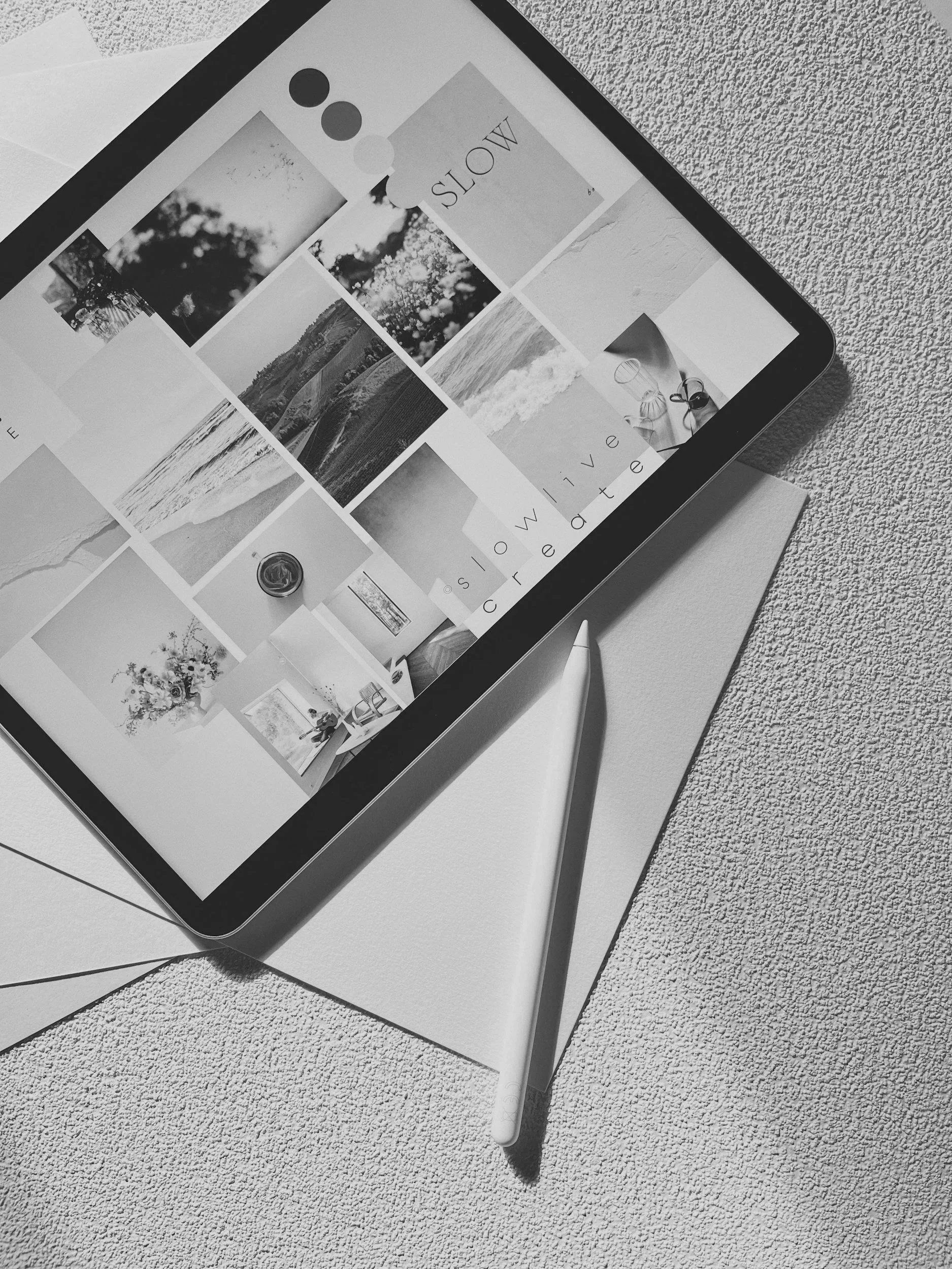 A digital tablet displaying a photo gallery with black and white images, resting on a textured surface with a white stylus pen next to it.