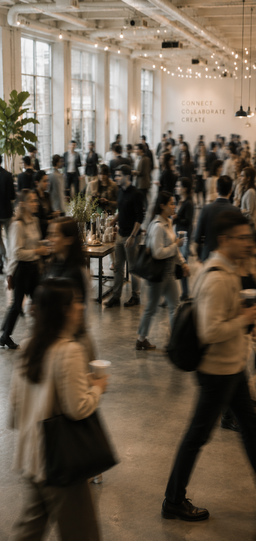 People mingling at a networking event in a bright, modern industrial space with large windows, string lights, and a sign on the wall that reads 'Connect, Collaborate, Create.'