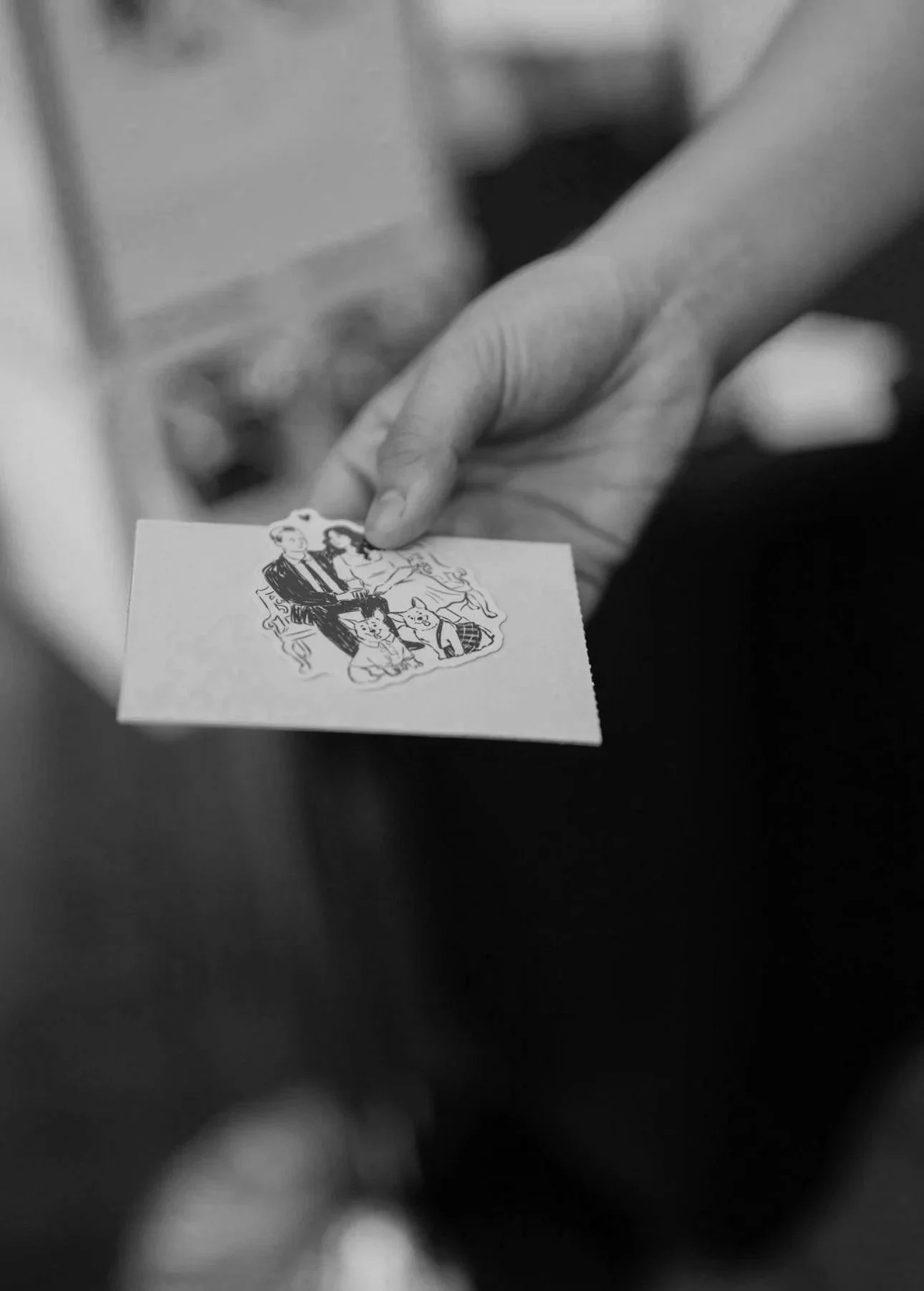 A person holding a small illustrated card with a drawing of a man and woman sitting together, surrounded by children.