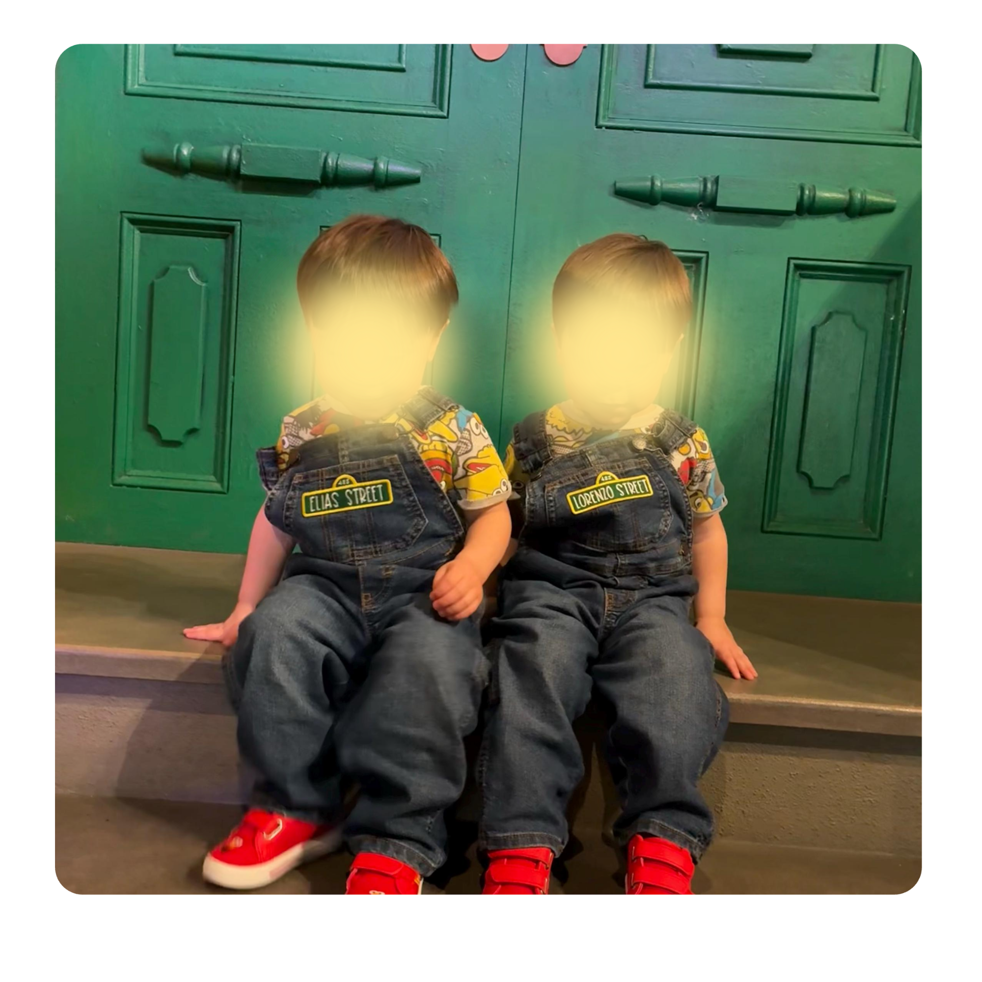 Two children sitting on a gray floor with their backs to the camera in front of a green door, wearing denim overalls with labels that read Elias Street and Lorenzo Street, red and white sneakers, and colorful shirts.