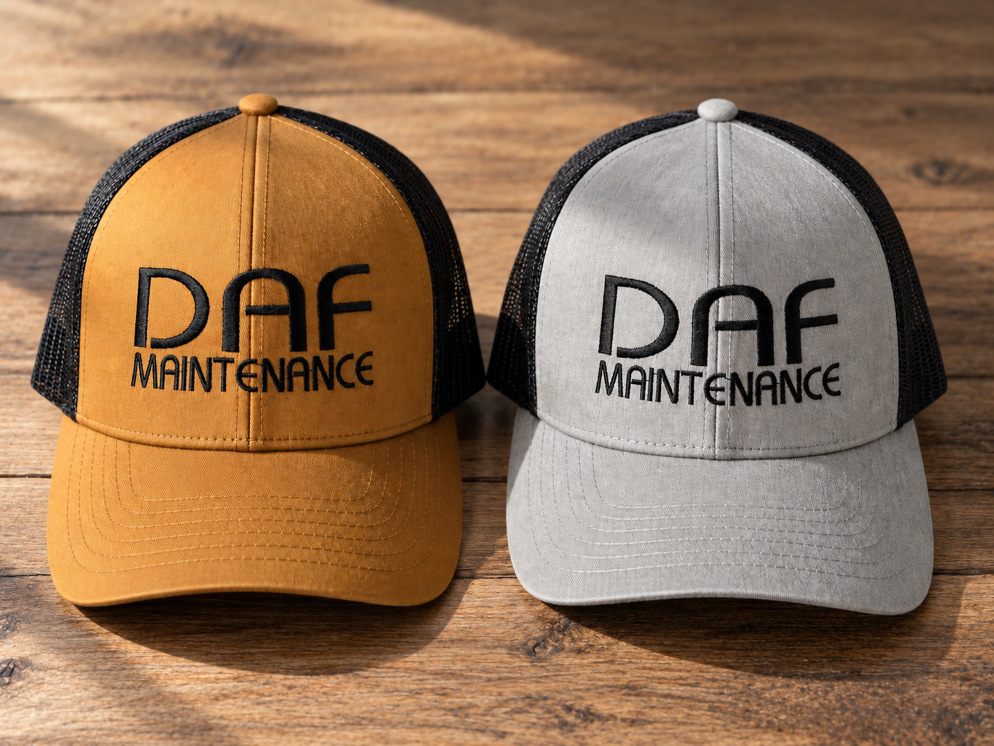 Two trucker-style baseball caps, one yellow and one light gray, both with black mesh backs and embroidered text reading 'DAF Maintenance' on the front, placed on a wooden surface.