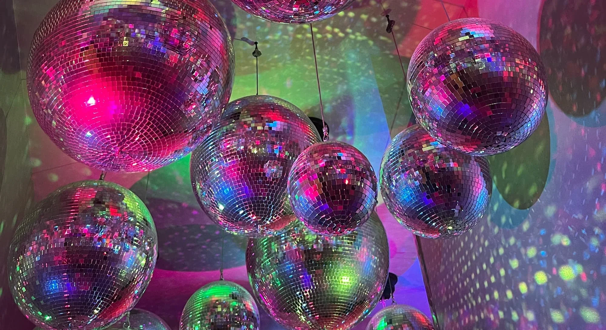 Multiple small disco balls hanging from the ceiling, reflecting colorful lights and creating a vibrant display of light and color on the walls and ceiling.