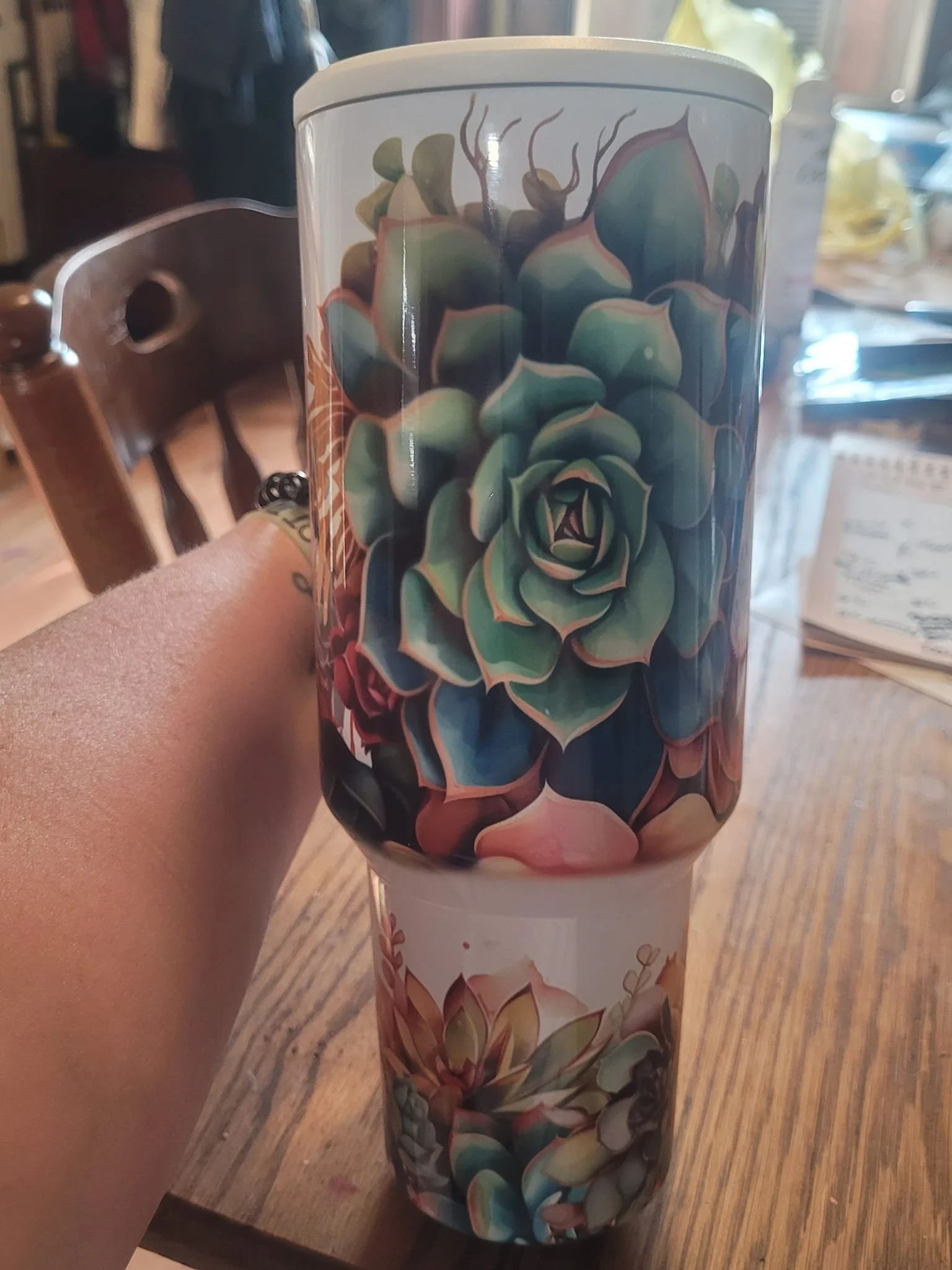 A close-up of a coffee mug with an illustration of a succulent plant on it, held by a person's hand.