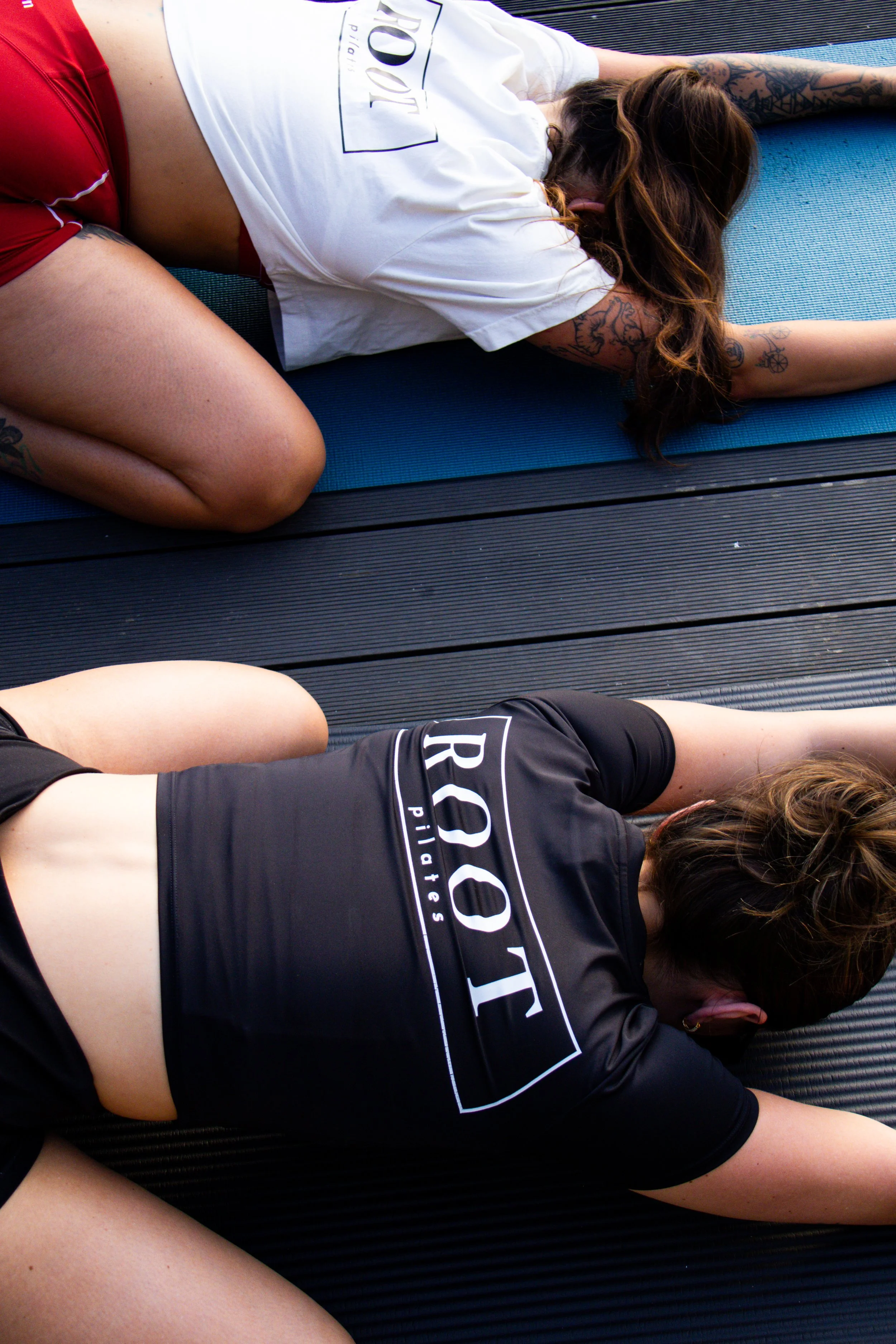 A woman lying on her side with her head resting on her arm on a blue yoga mat outdoors.