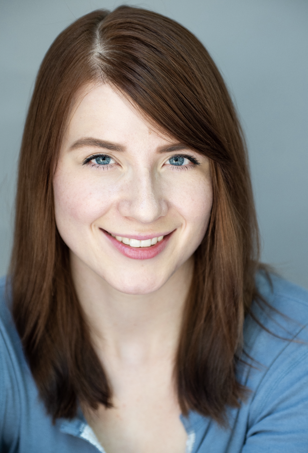 Close-up of a smiling young woman with red hair and blue eyes, wearing a blue top.