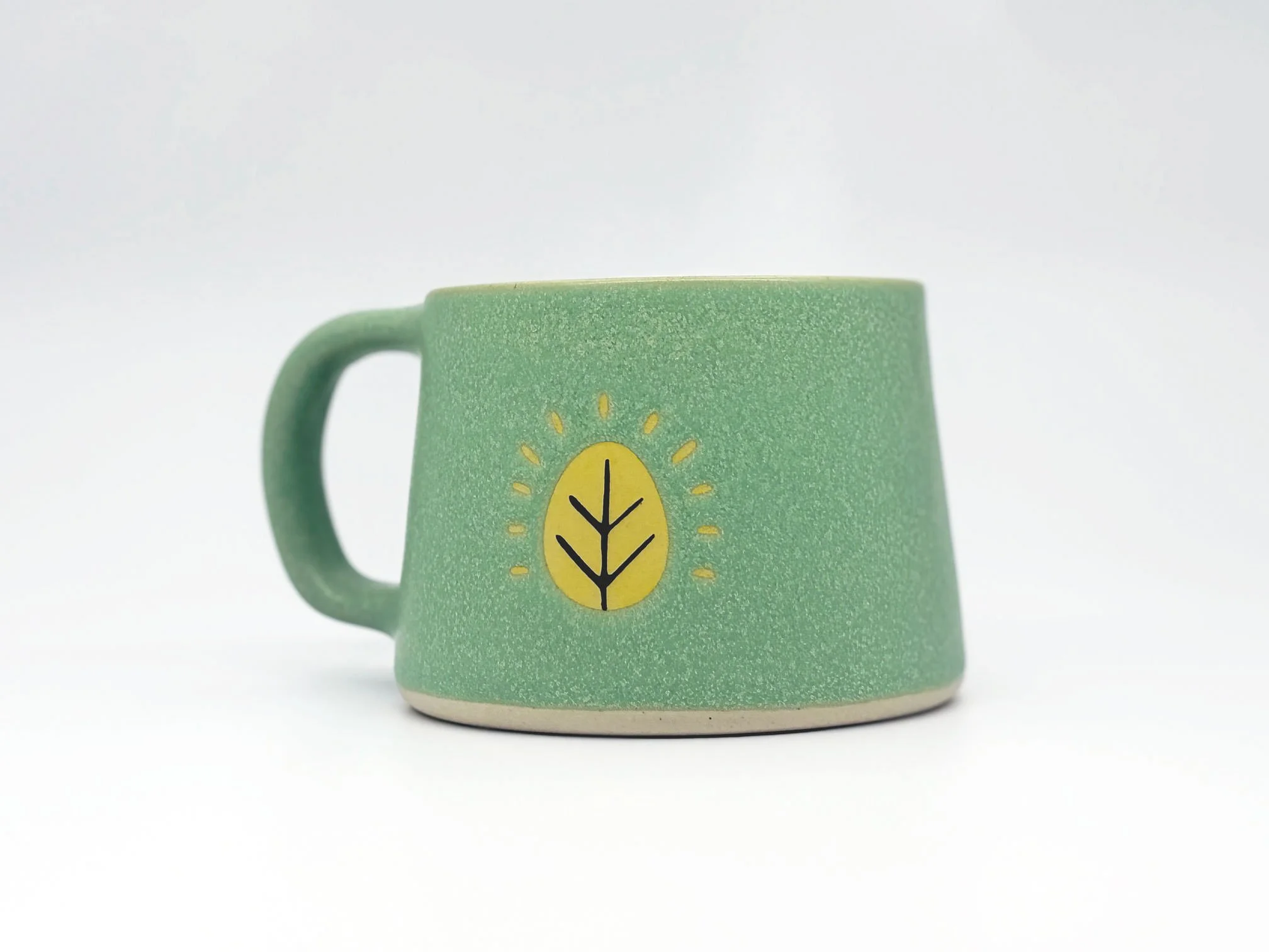 Sugar Leaf ceramic coffee mug, teal with the brand's yellow leaf mark