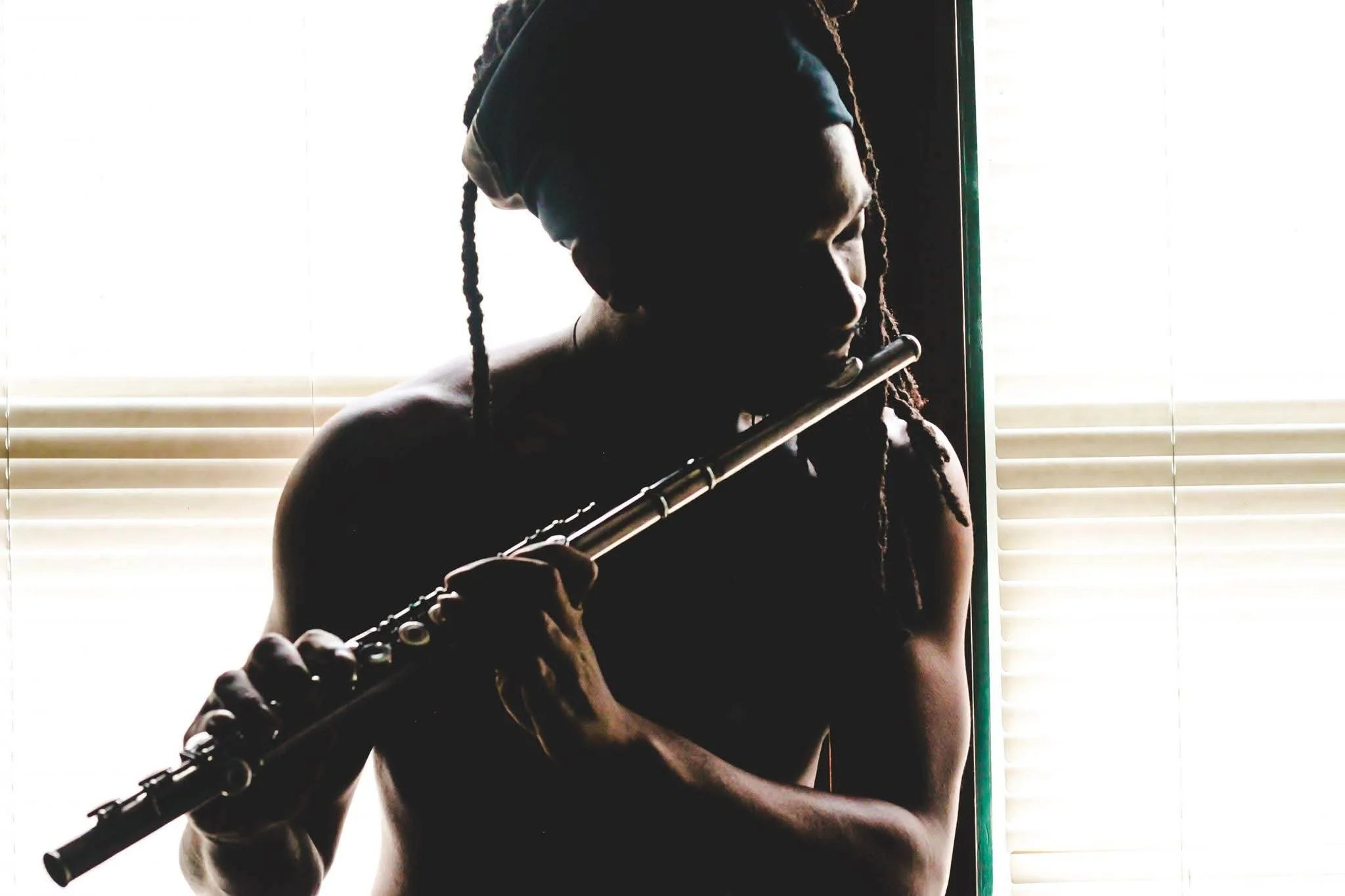 Person playing a flute with blinds in the background.