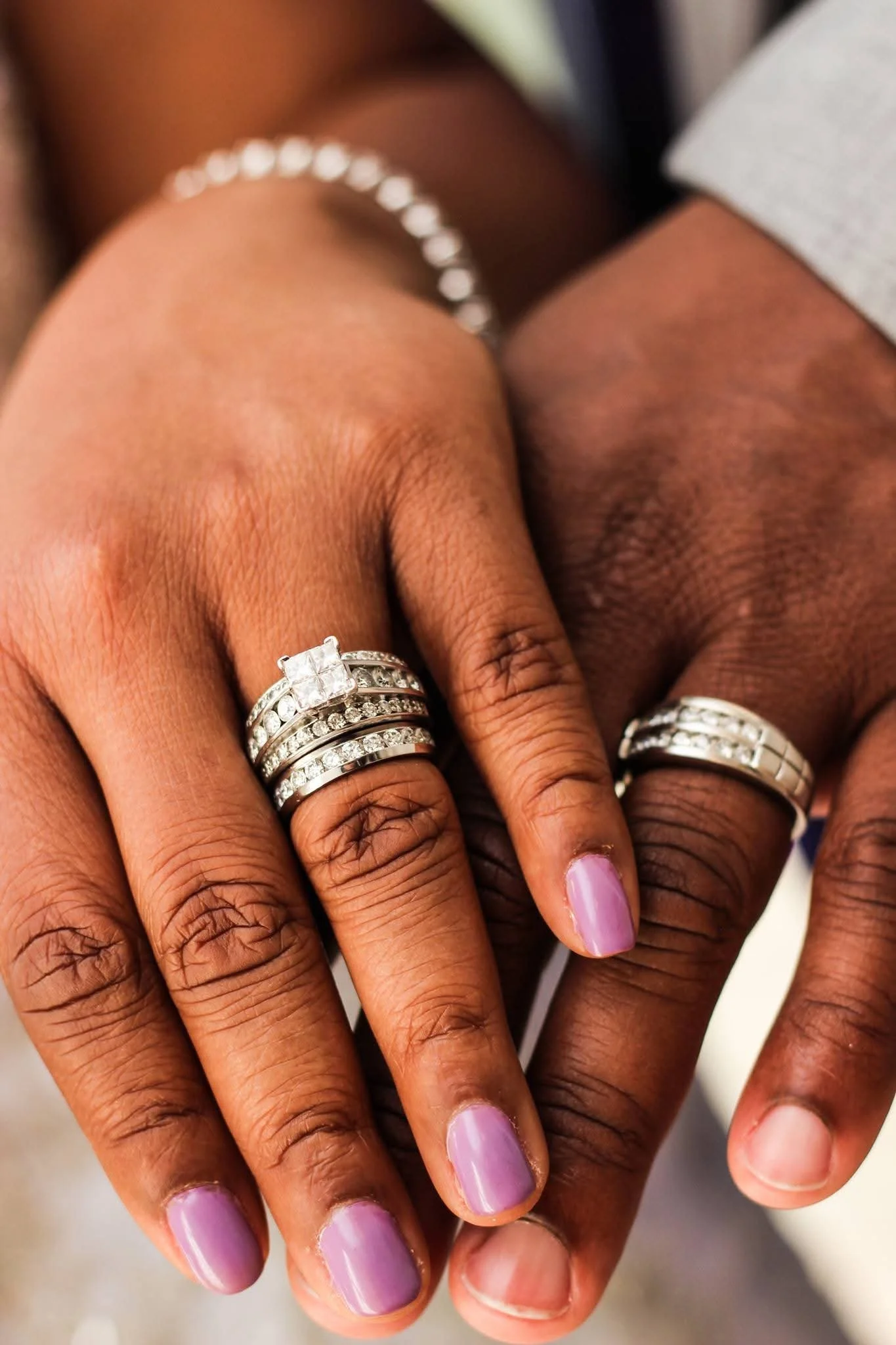 Close-up of two hands with multiple diamond rings, adorned with light pink nail polish.