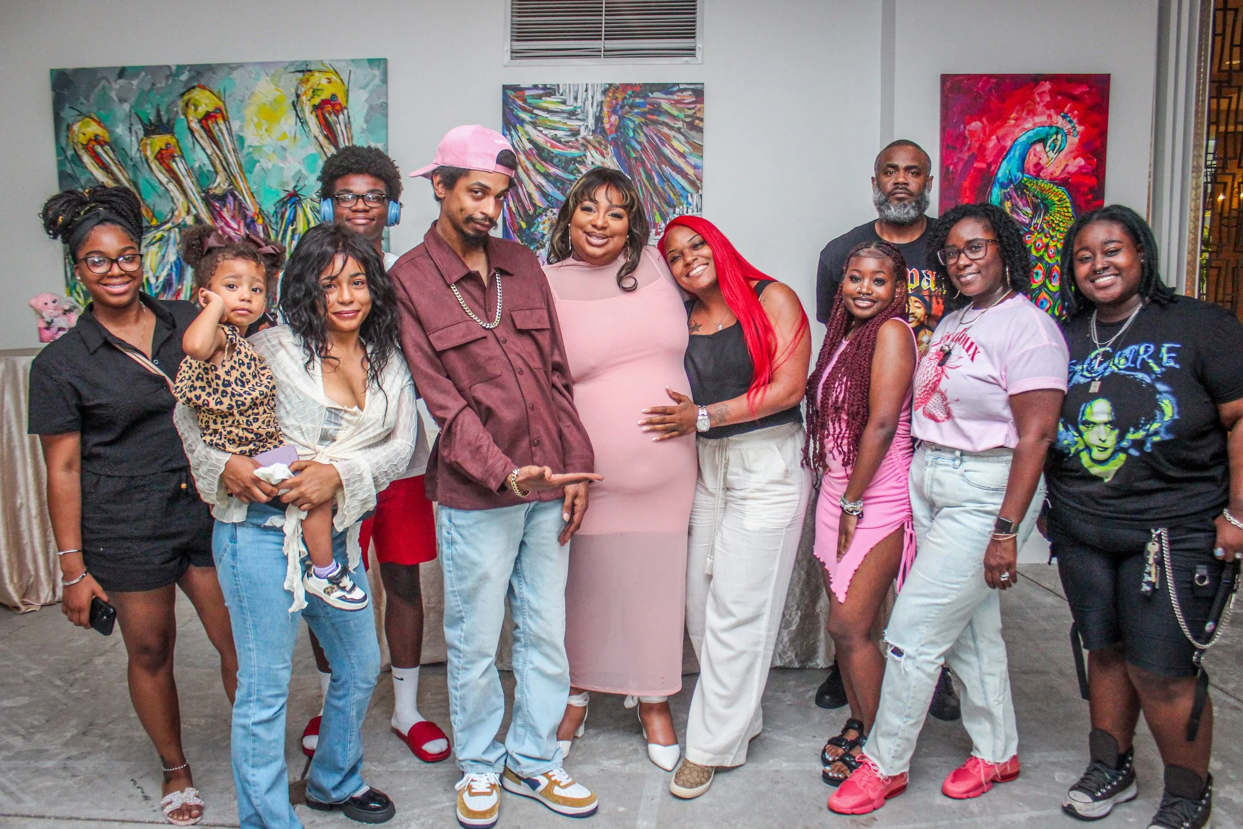 A diverse group of people standing together indoors in front of colorful abstract paintings, smiling at the camera.