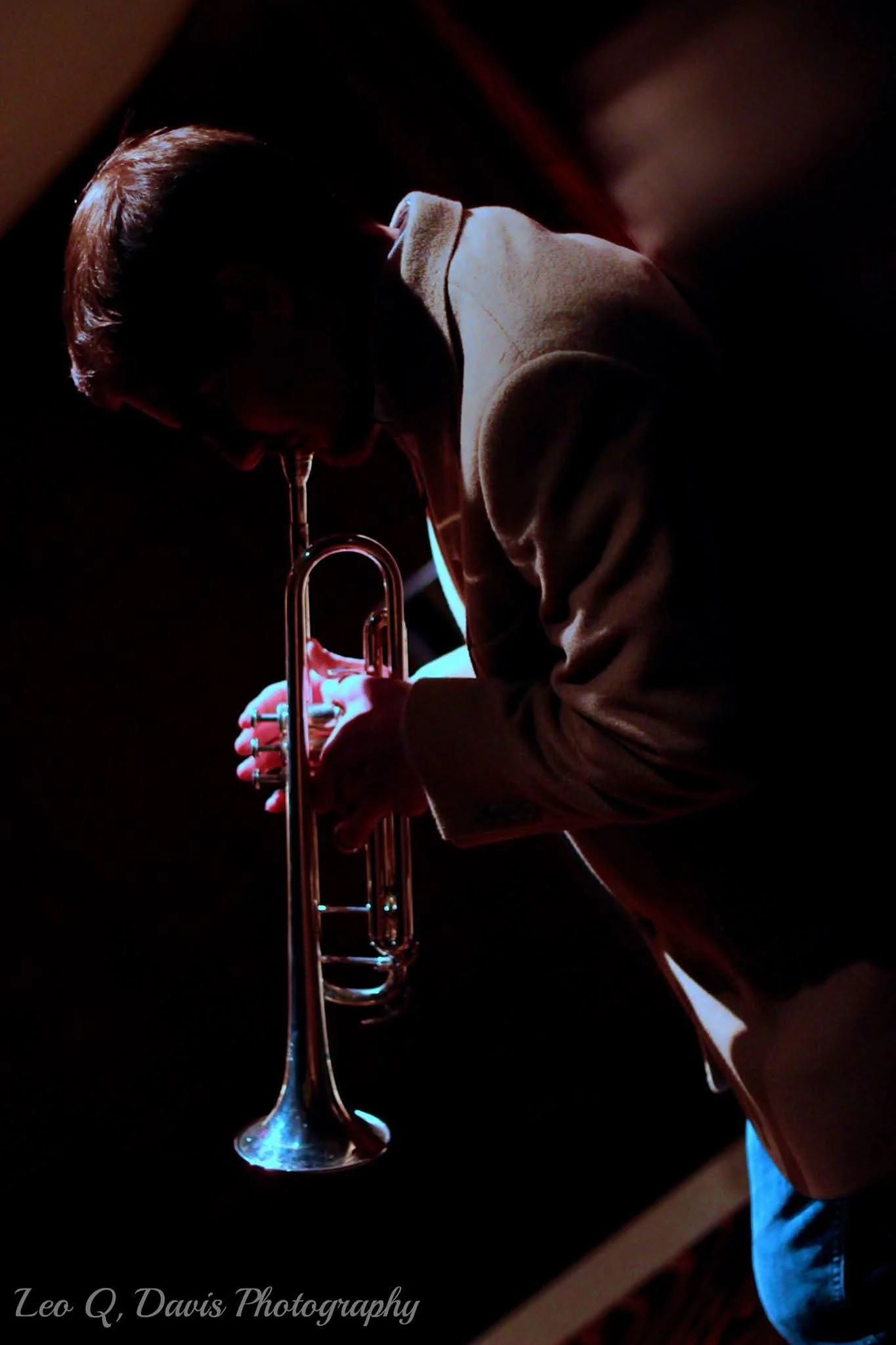 A person holding a trumpet in a dark setting, with a focused light highlighting the instrument.