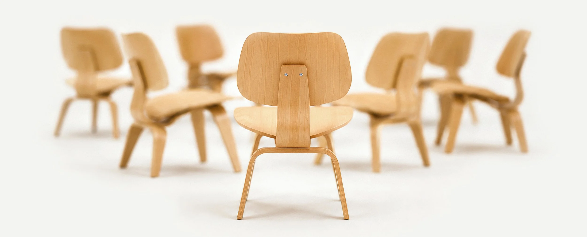A grouping of empty, modern wooden chairs with a single chair, in-focus in the foreground.