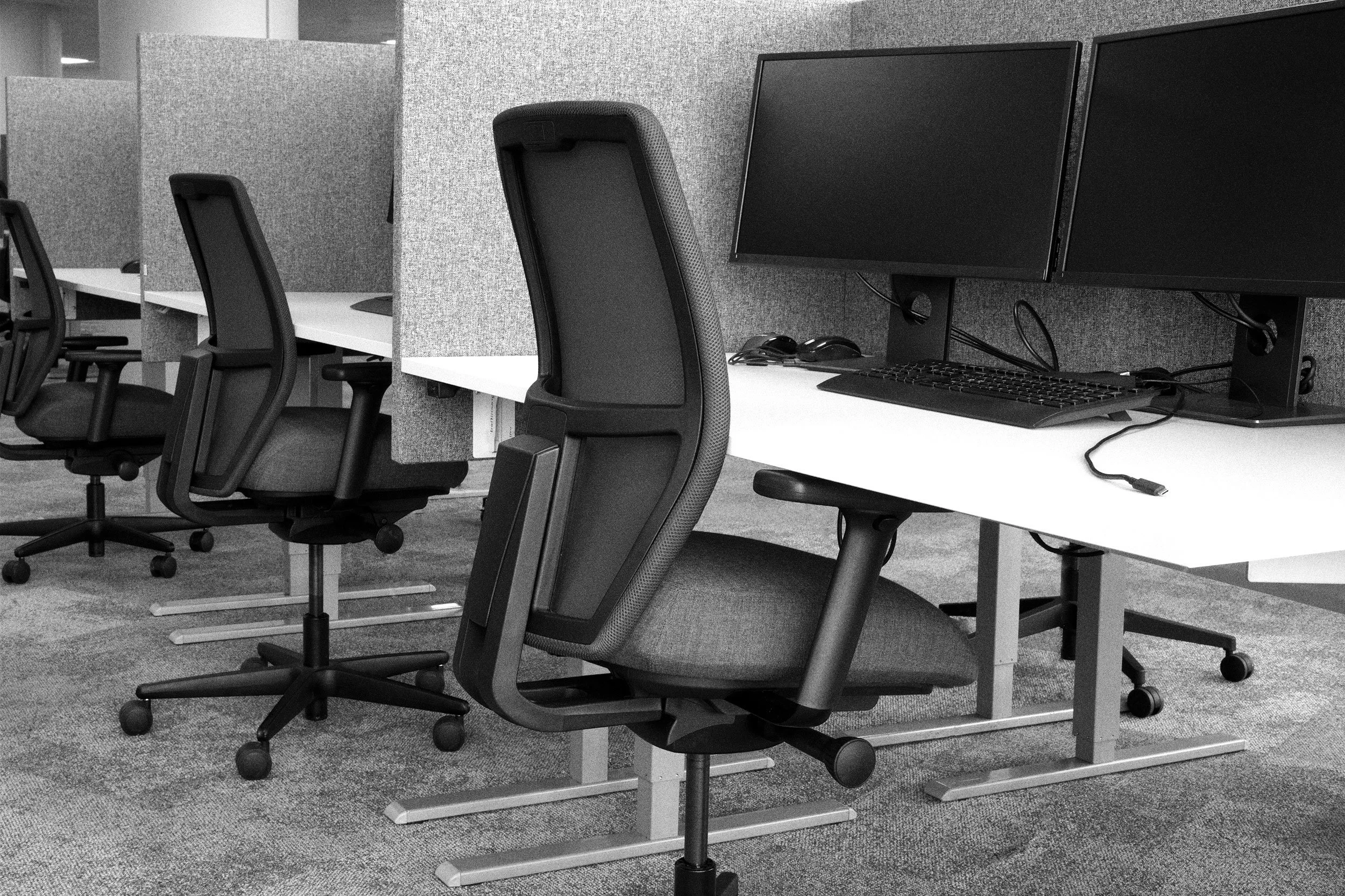 Office workspace with ergonomic chairs, computer monitors, and cubicle partition walls in black and white.