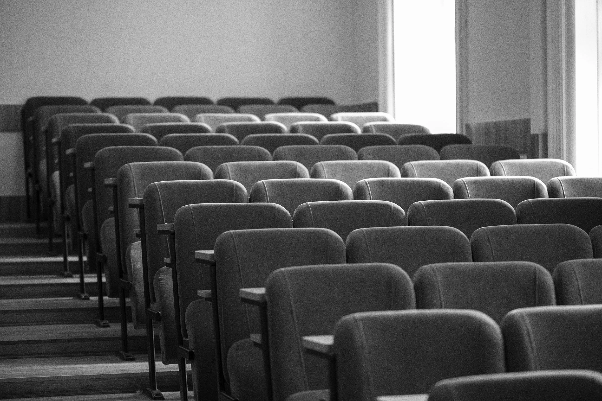 Empty auditorium with rows of chairs and a large window letting in natural light.