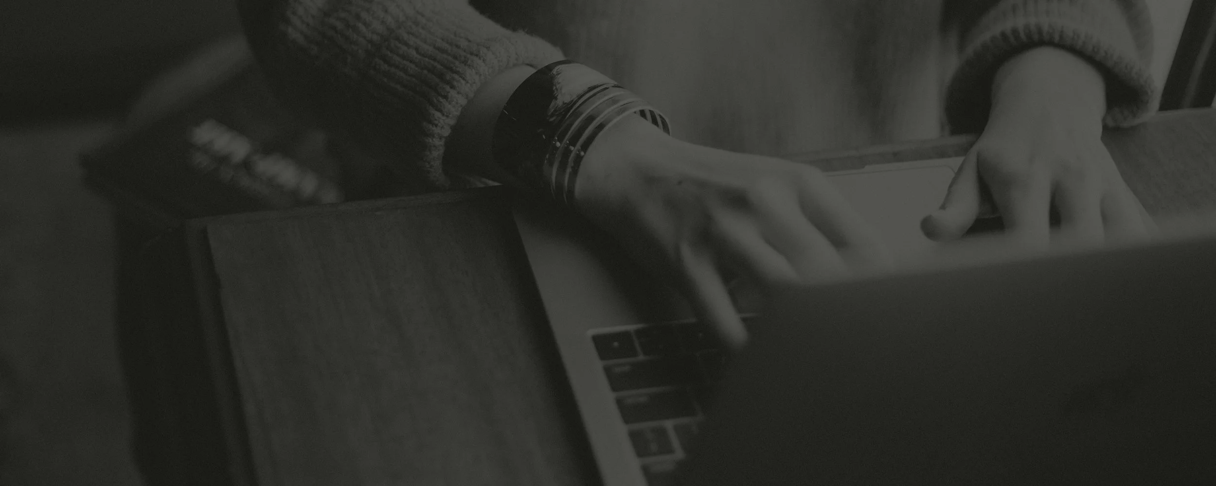 Black and white photo of hands typing on a laptop keyboard with a coffee mug nearby.