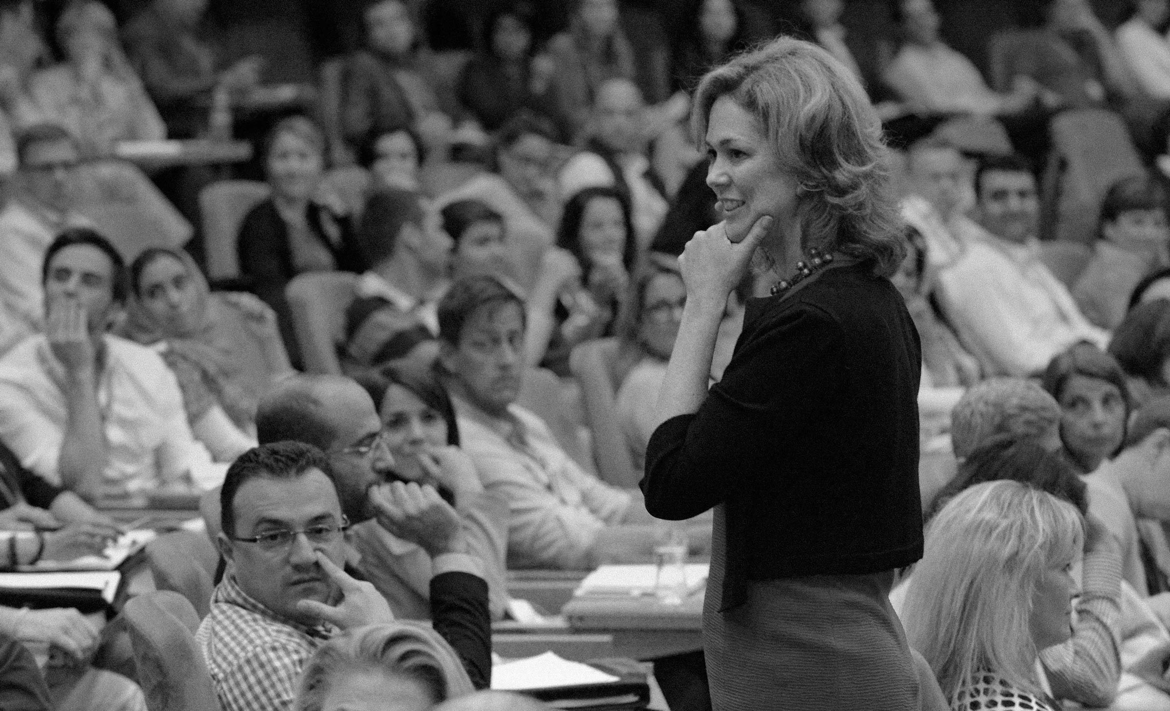 Sheila Heen stands with her hand on her chin, speaking to an audience in a large room, with many seated listeners paying attention.