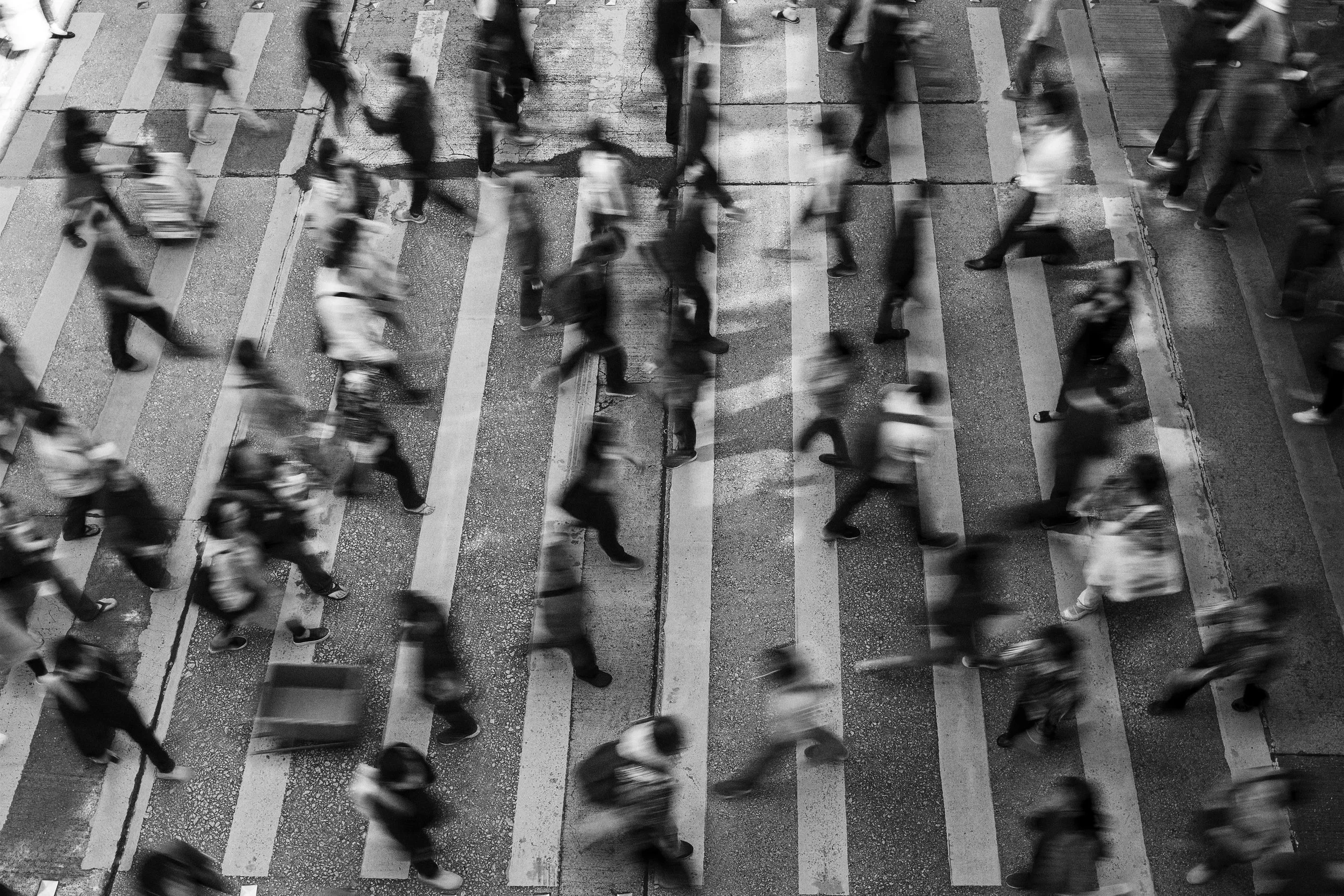 Black and white aerial view of people crossing a city street at a crosswalk.