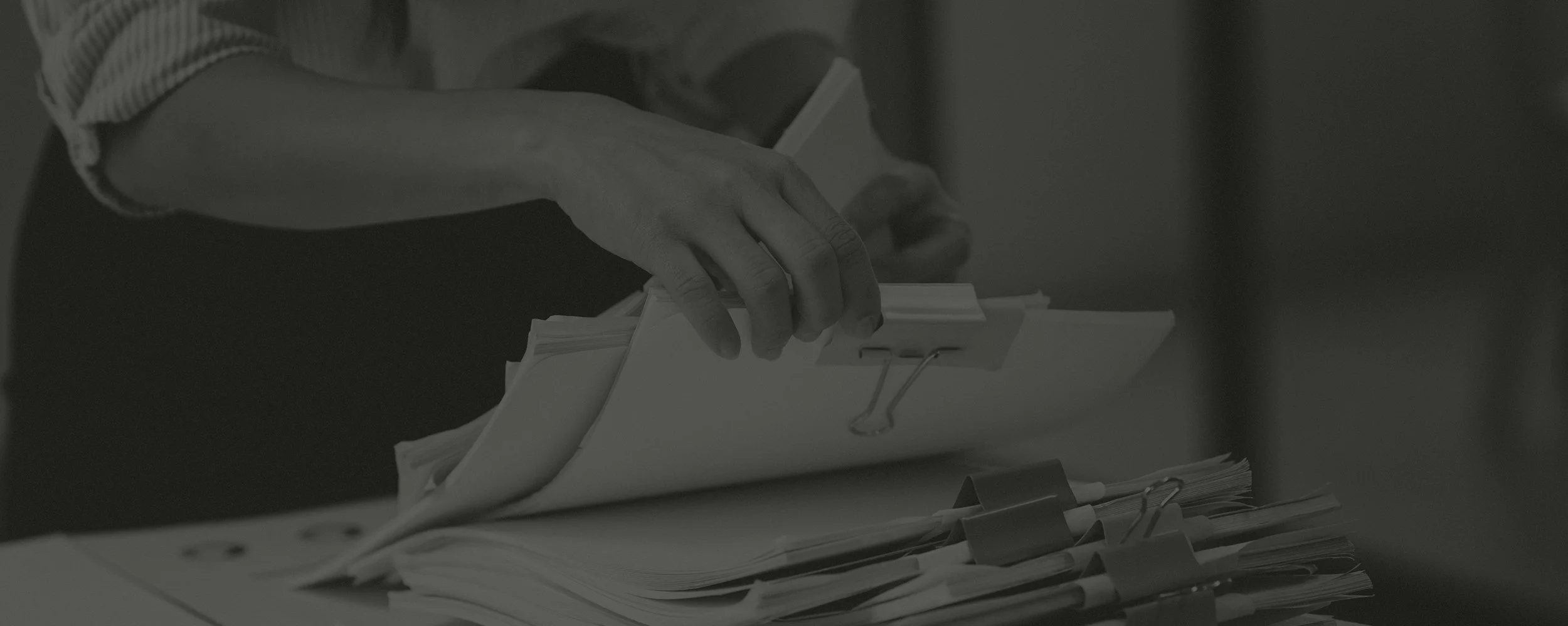 Close-up of a person's hand flipping through a binder filled with papers, with additional papers and clips on the table.