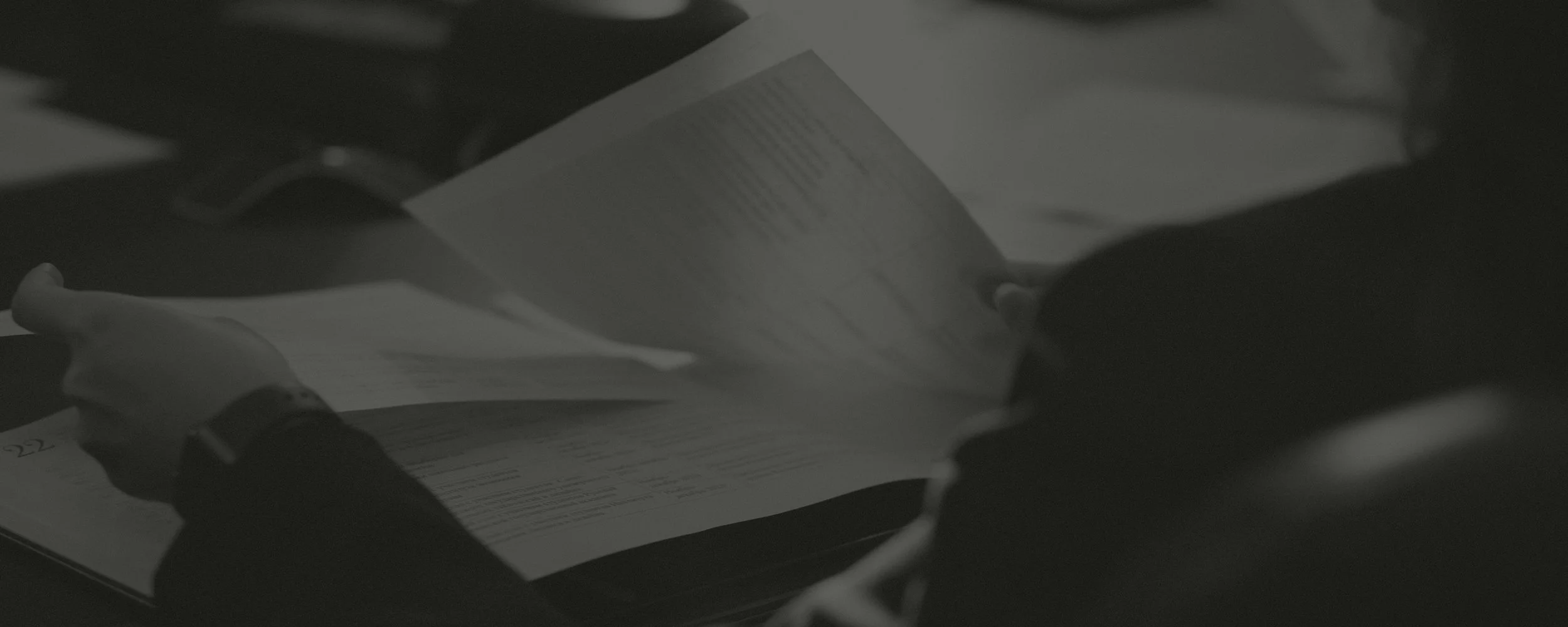 Person reading papers at a desk in a dimly lit environment.