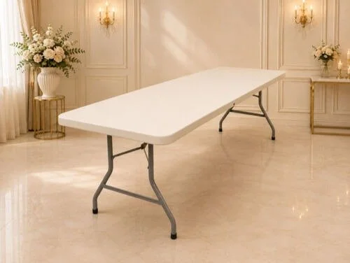 Empty white folding table in an elegantly decorated room with floral arrangements and wall sconces.