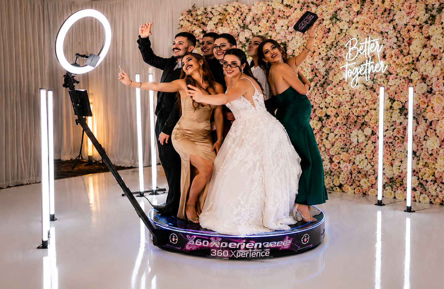 Group of women and one man taking a selfie at a wedding with a floral backdrop and a sign that says 'Better Together.'