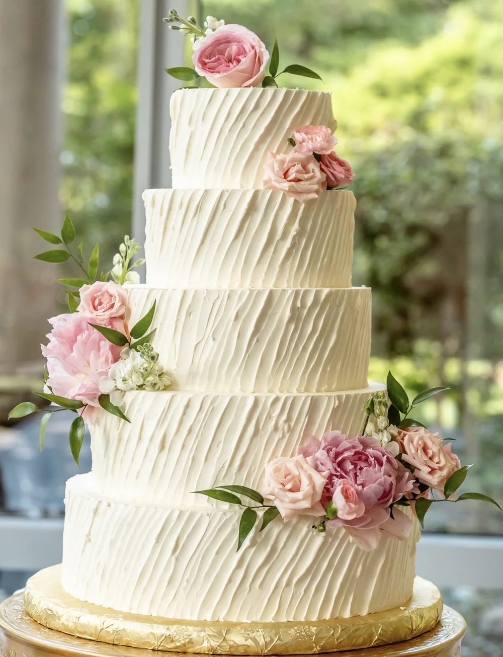 A white tiered cake with textured icing and pink flowers.