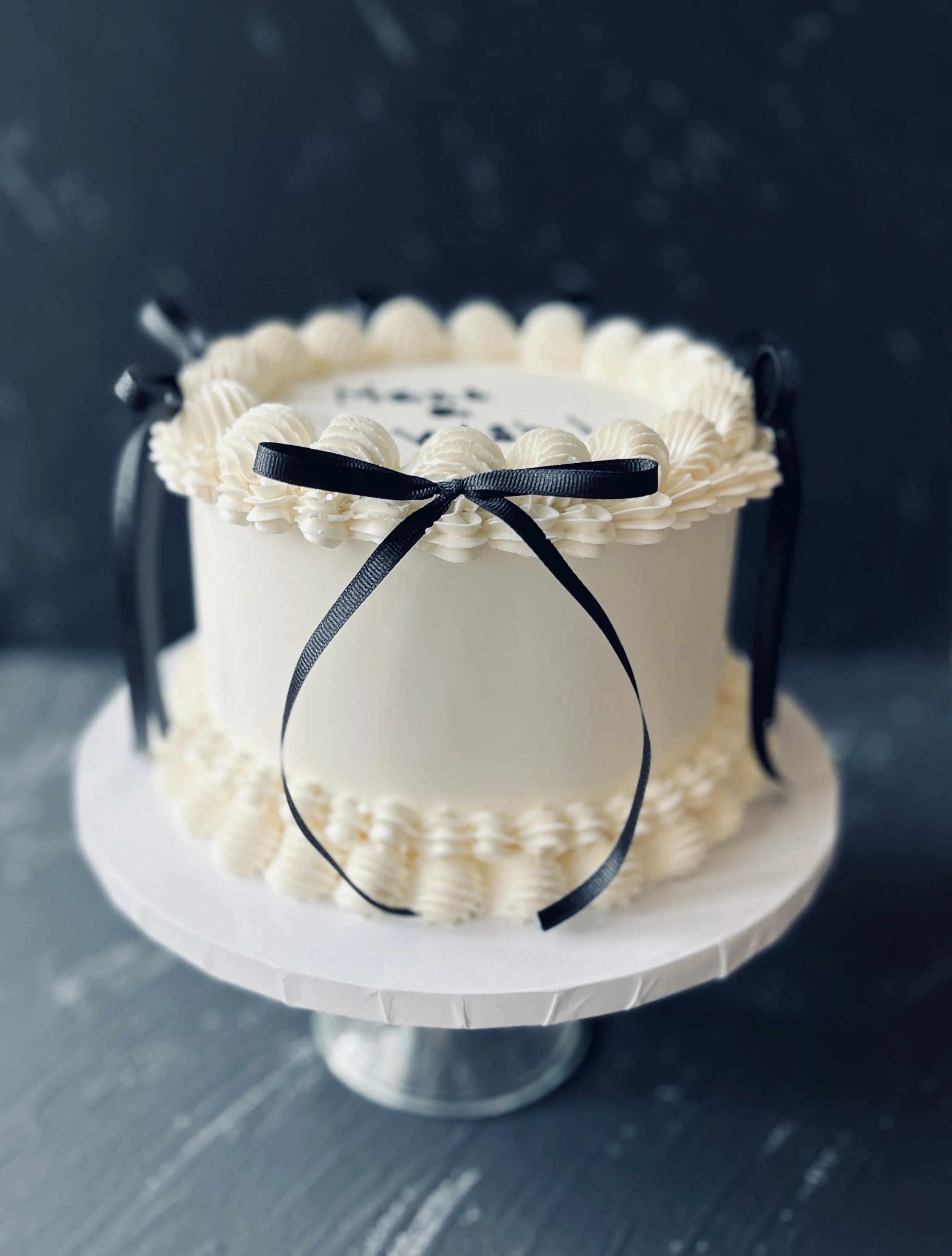 White cake with piped borders and a dark ribbon bow.