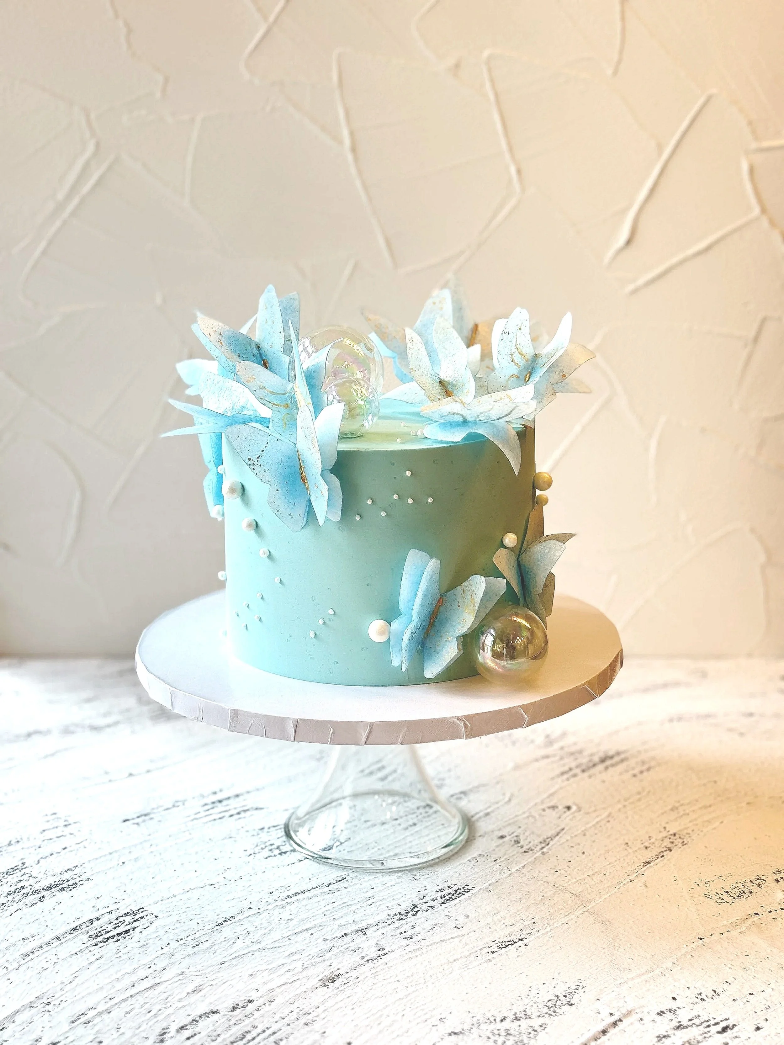 Pale blue cake with white drips and blue and white leaf-like decorations.