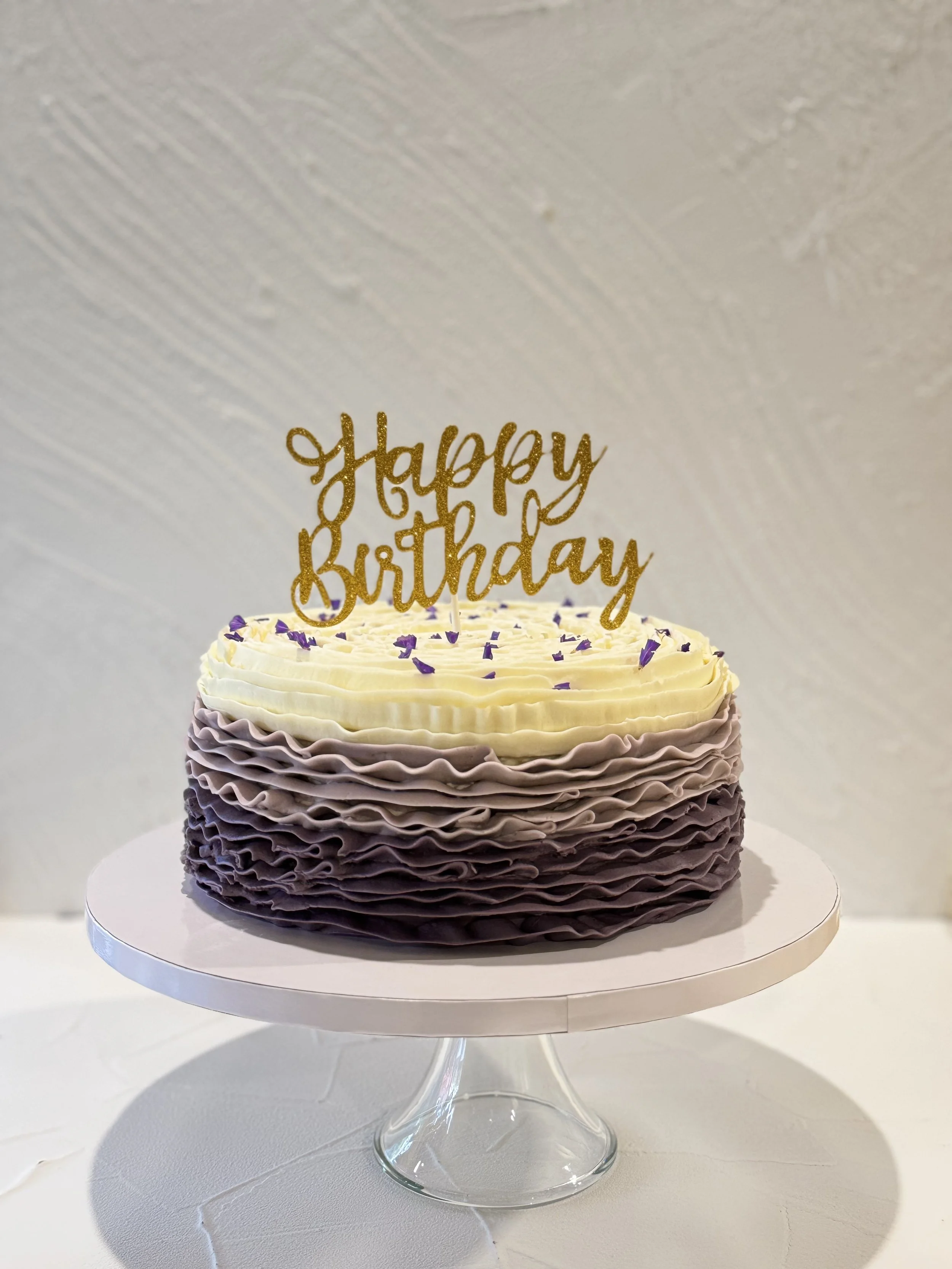 Dark layered cake with pale piped edging and a gold birthday topper.