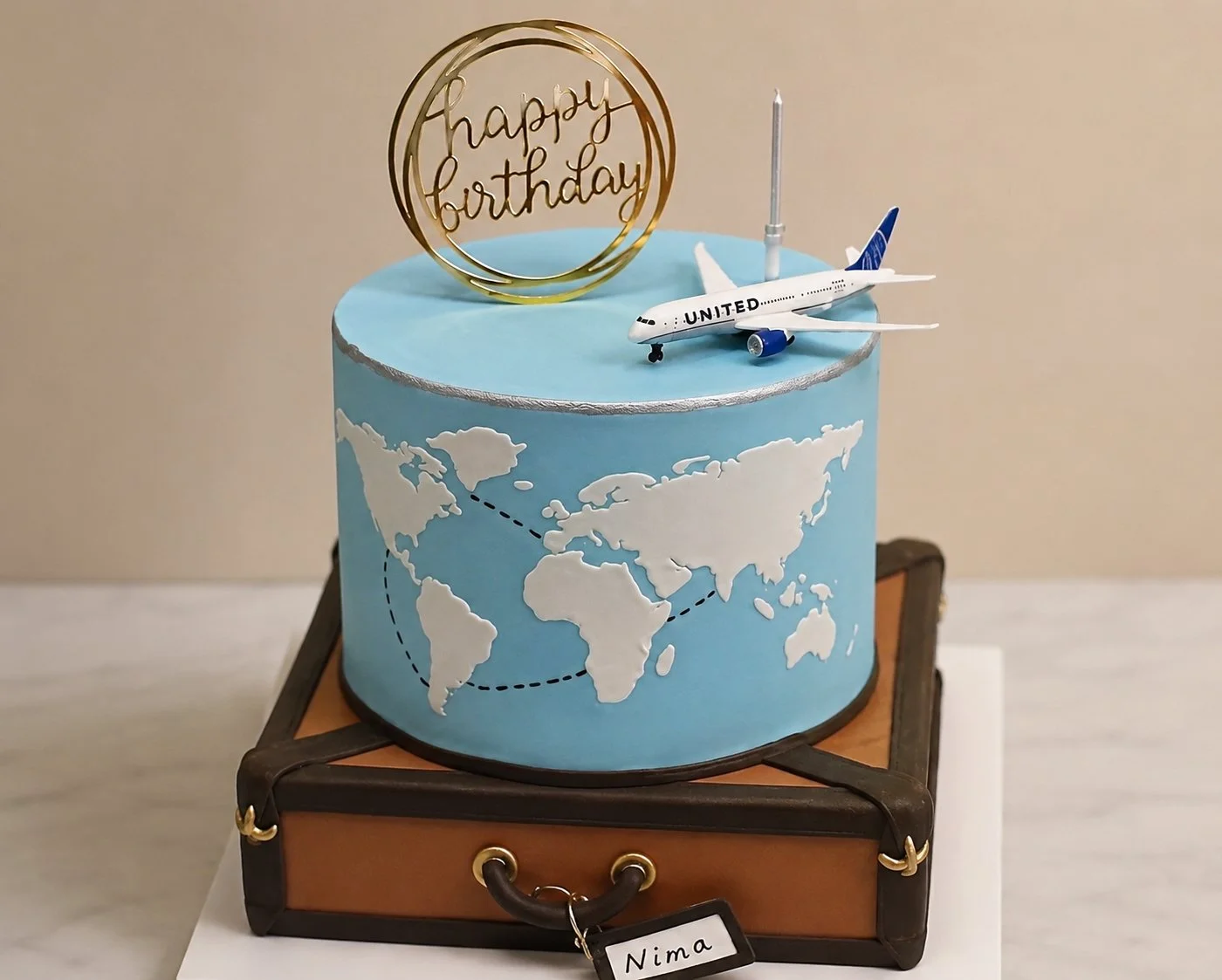 Blue world-map cake with an airplane topper on a suitcase-style base.