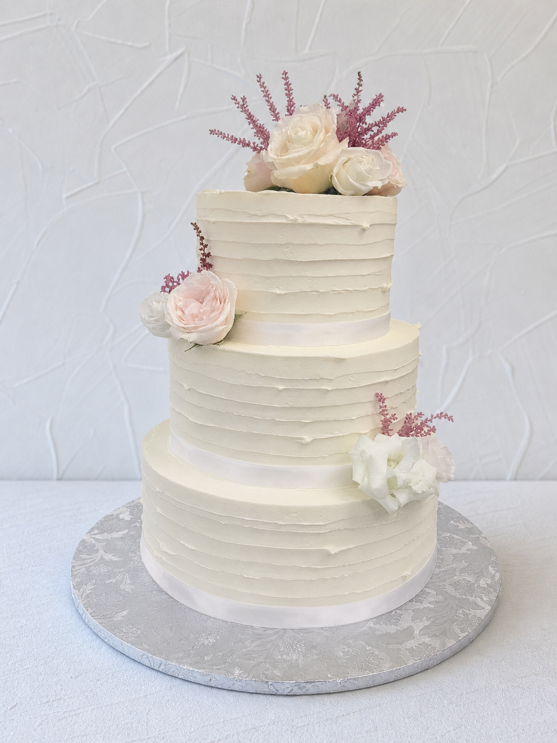 White tiered cake with horizontal texture and pale flower decorations.