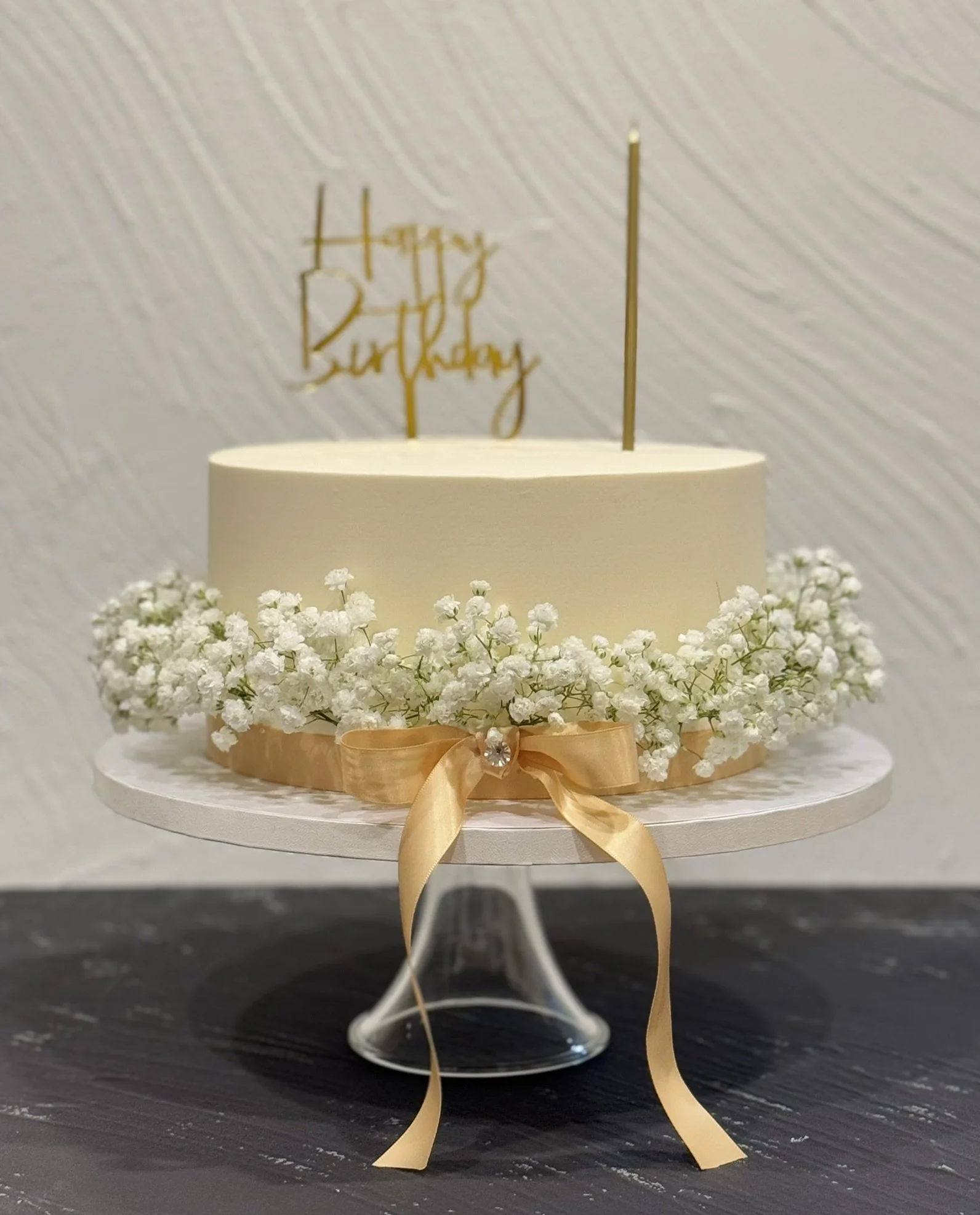 White cake with a band of small flowers and a gold birthday topper.