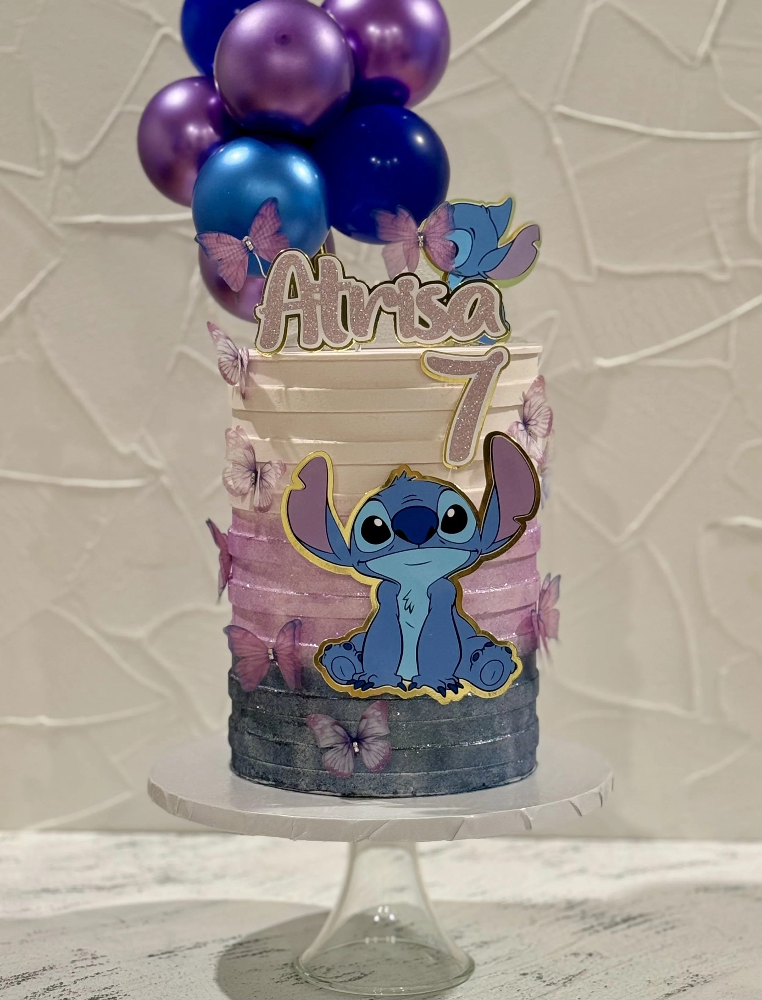 Blue and purple cake with butterfly decorations and balloon-like toppers.