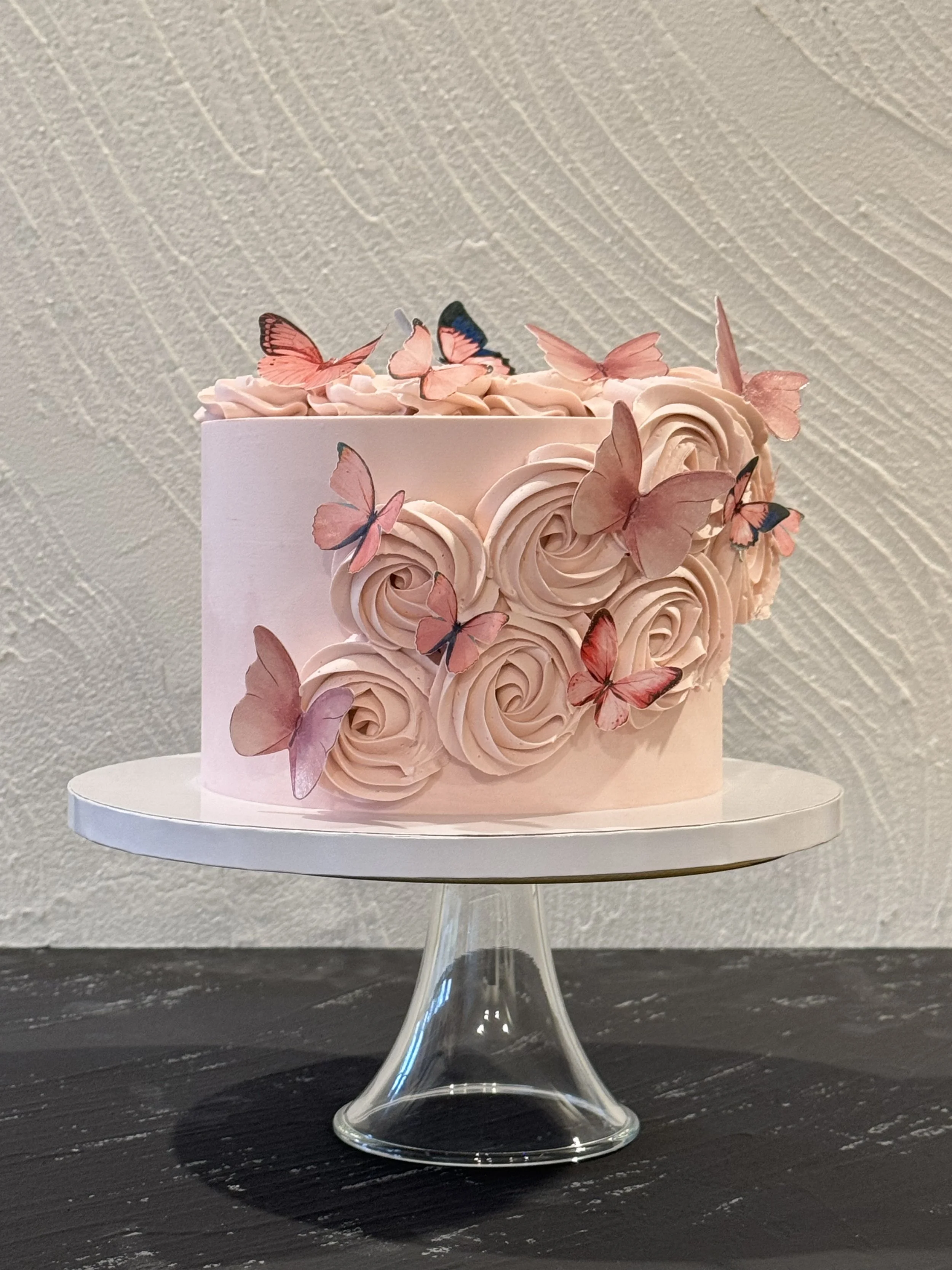 Pink cake with piped swirls and large pink floral decorations.