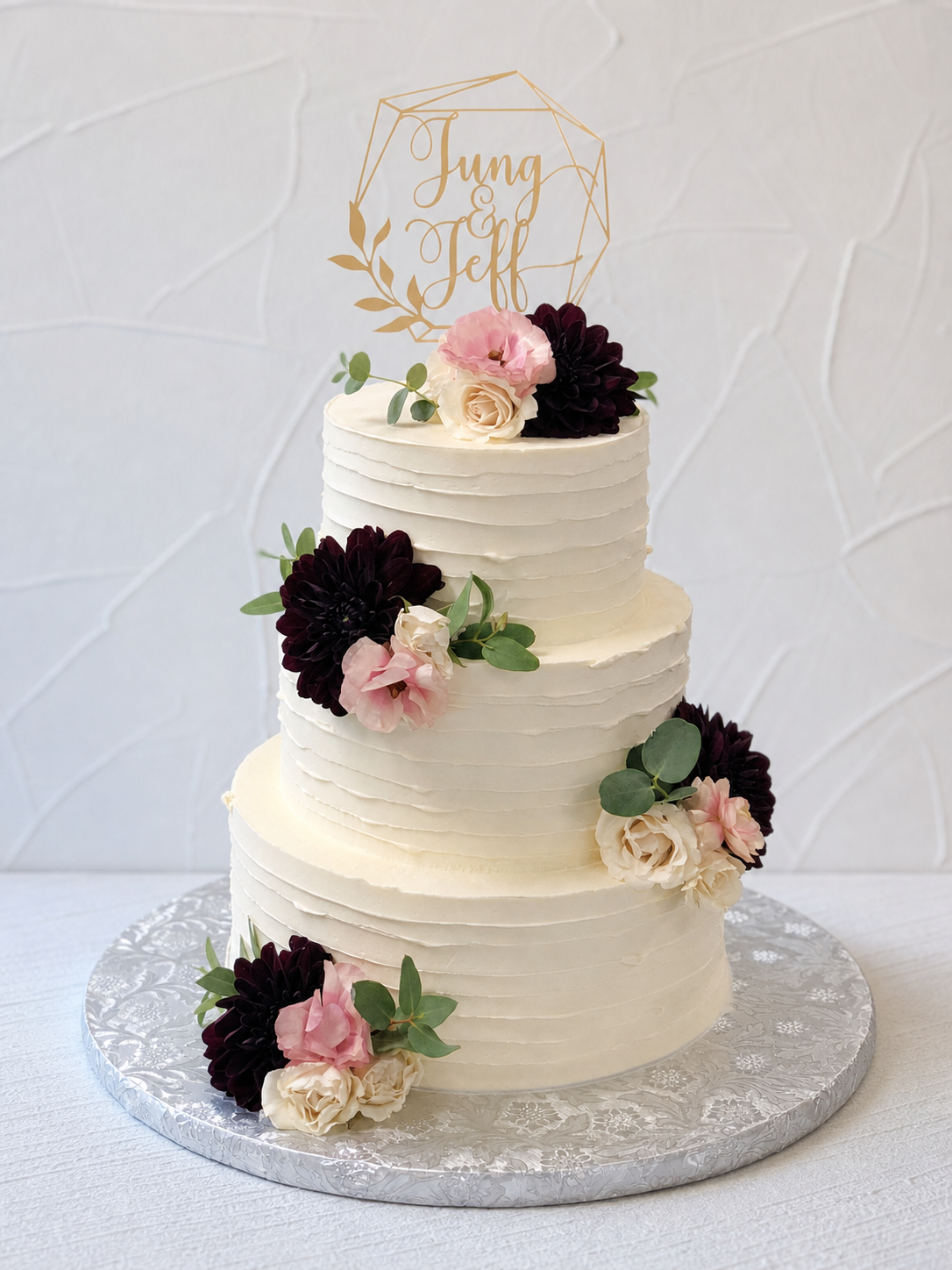 White tiered cake decorated with dark and pale pink flowers.