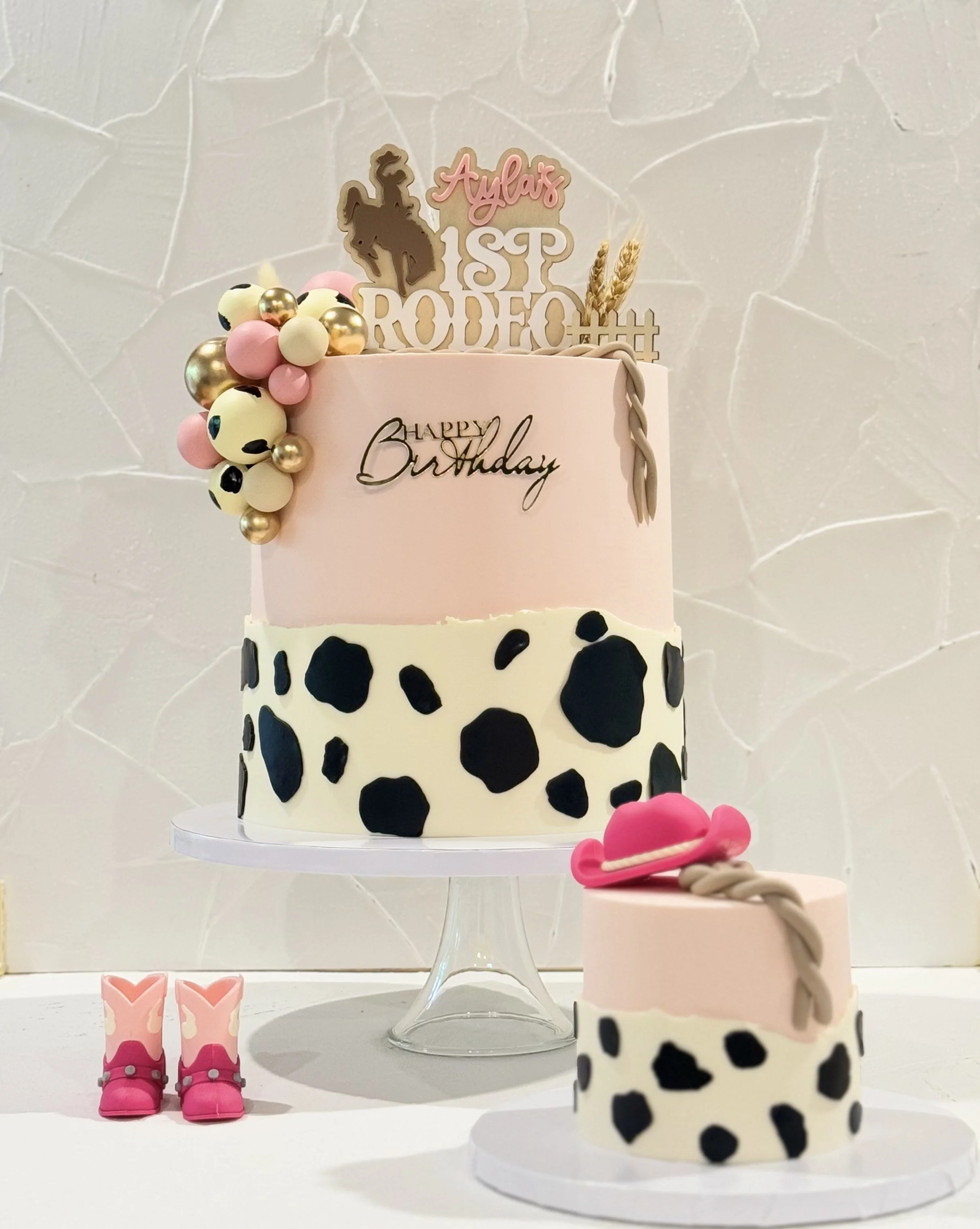 White cake with black spots, pink details, flowers, and gold decorations.