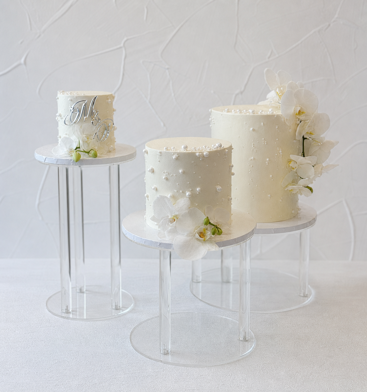 White cakes displayed on separate clear stands.